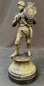 CAST METAL STATUE ON A WOODEN PLINTH OF A KNIGHT WITH SWORD AND SHIELD WITH CREST, 14.25IN TALL