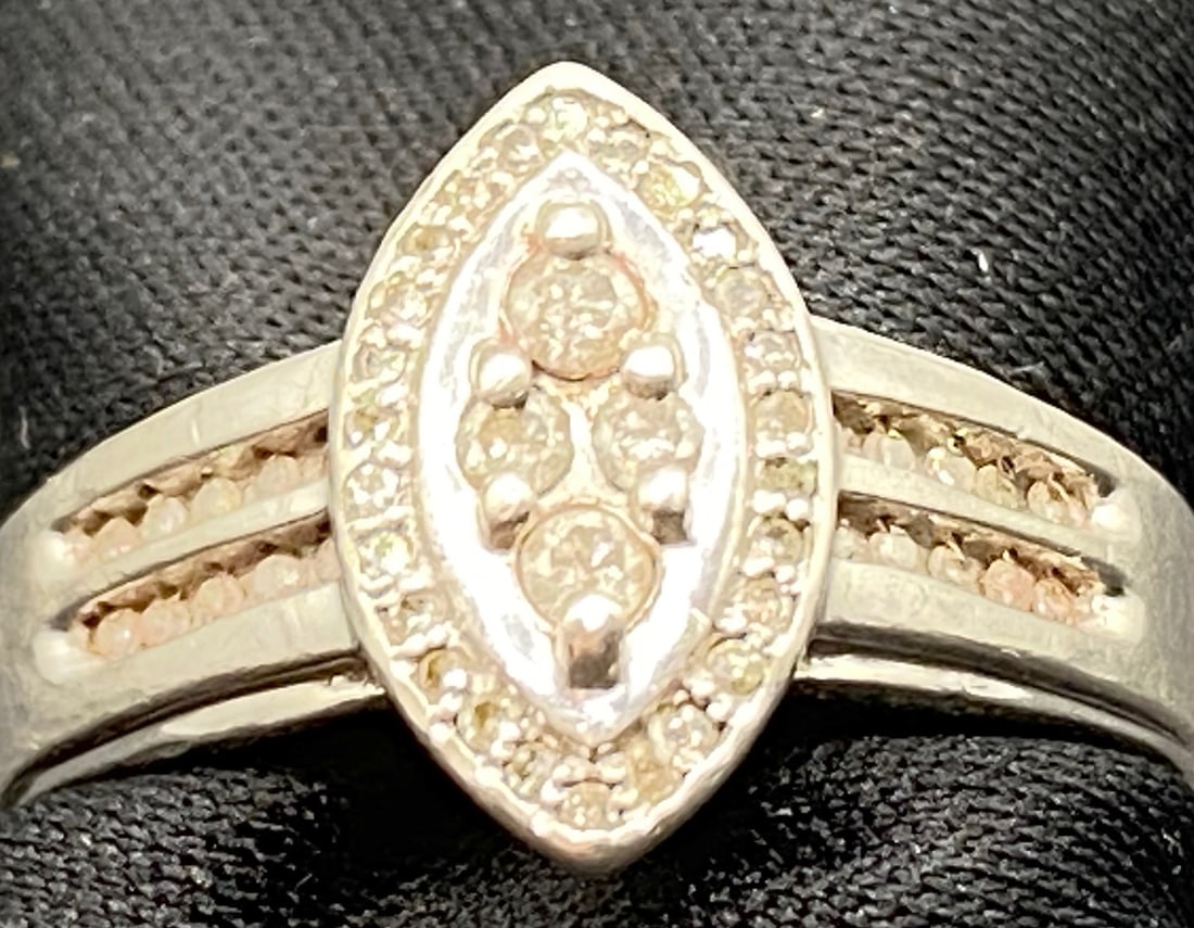 STERLING AND DIAMOND RING: Sterling silver and diamond ring. It features 4 genuine, round cut diamonds in the center. These are surrounded by an oval ring of 26 round cut diamonds. On either side of the ring there are 2 rows of