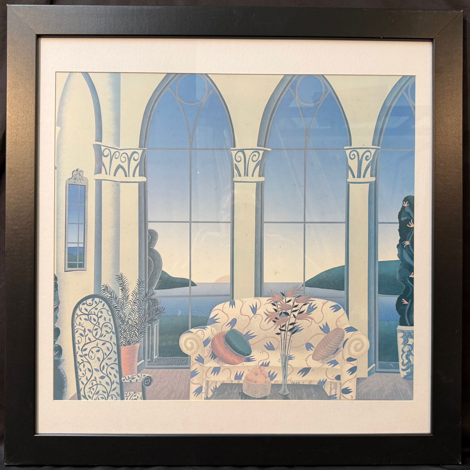 THOMAS MCKNIGHT (1941) SERIGRAPH TITLED FLOWERED COUCH, 29.5IN x 29.5IN (75cm x 75cm): Serigraph on paper by American artist Thomas McKnight (1941) is titled Flowered Couch, and the image depicts a vibrant, stylized interior room with gothic-style windows looking out over a blue body of