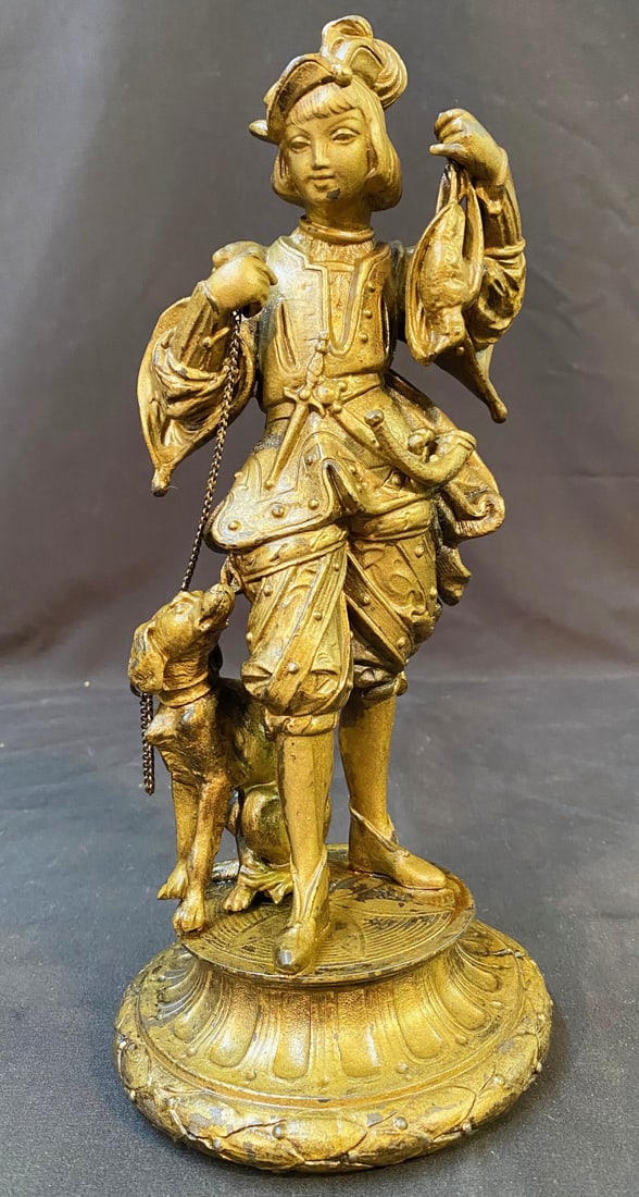SPELTER FIGURINE STATUE OF A HUNTER WITH DOG, 12IN TALL (30.5cm): Spelter Figurine statue of a hunter with a dog. It depicts a man in elaborate period attire holding game birds and a rifle, with a hunting dog by his side. This piece was acquired from a Virginia esta