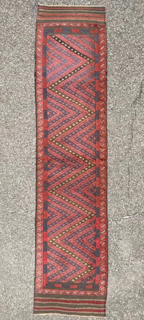 VINTAGE TRIBAL MASHWANI HAND KNOTTED RUNNER, 2.0 x 8.3 (61cm x 251cm): A striking and highly versatile tribal Mashwani runner distinguished by its bold, rhythmic chevron (zig-zag) pattern, rendered in a rich palette of brick red and deep indigo tones. This piece is 50+ y