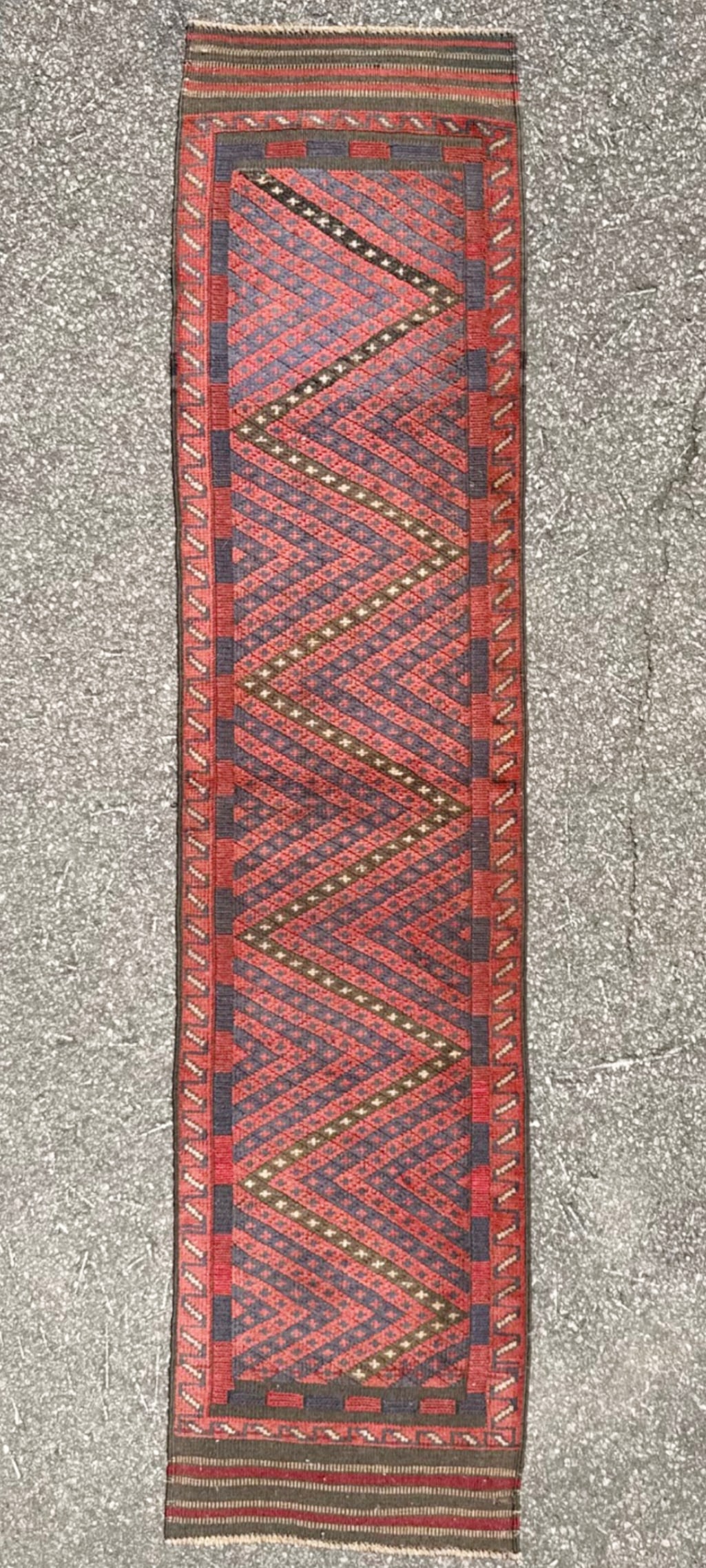 VINTAGE TRIBAL MASHWANI HAND KNOTTED RUNNER, 2.0 x 8.3 (61cm x 251cm): A striking and highly versatile tribal Mashwani runner distinguished by its bold, rhythmic chevron (zig-zag) pattern, rendered in a rich palette of brick red and deep indigo tones. This piece is 50+ y