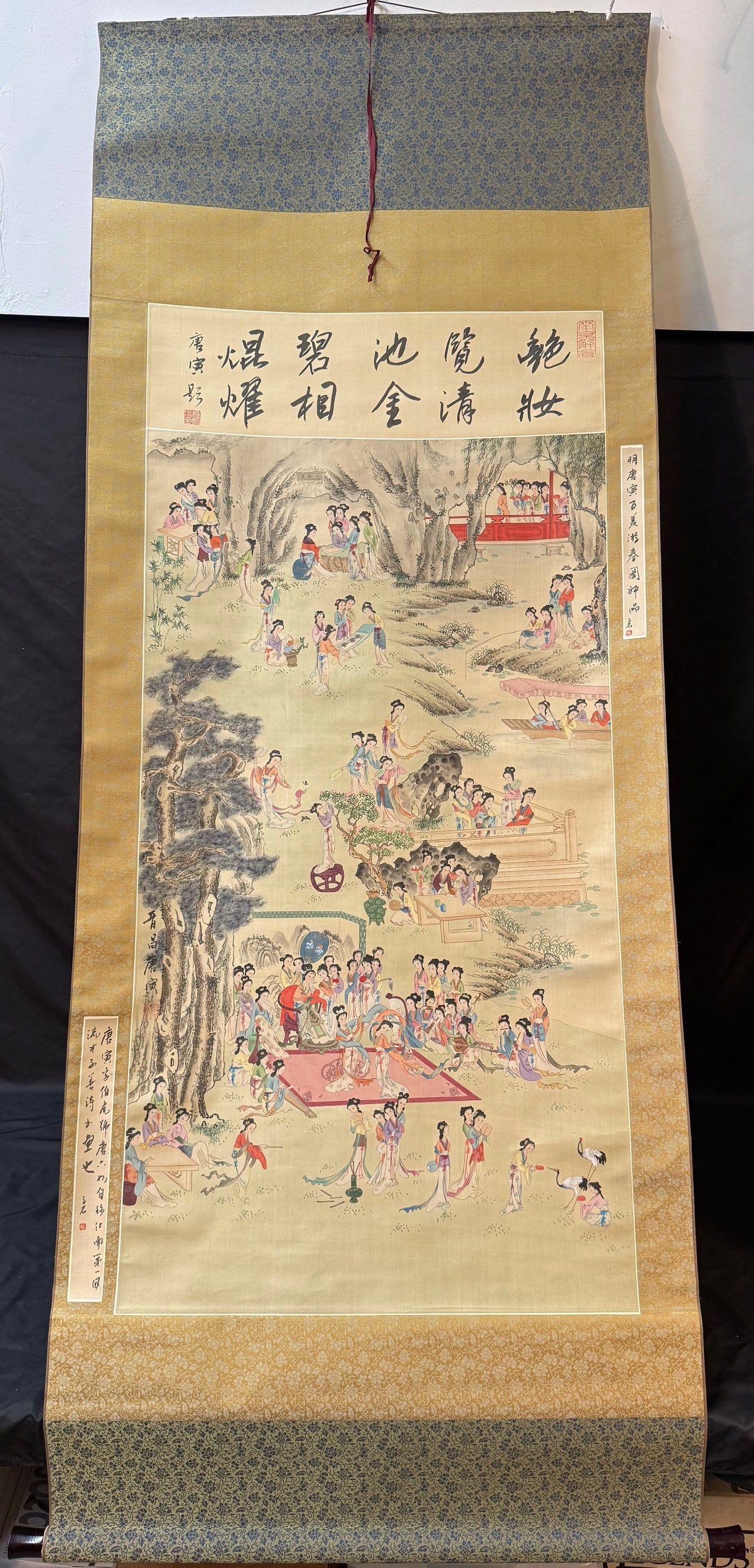 ANTIQUE CHINESE SCROLL PAINTING OF COURT LADIES JN A GARDEN PAVILLION, 30IN x 78IN (76cm x 198cm): A finely detailed Chinese figural painting depicting an elegant gathering of court ladies (shinu hua) within a lush garden landscape, rendered in ink and mineral pigments on silk and mounted