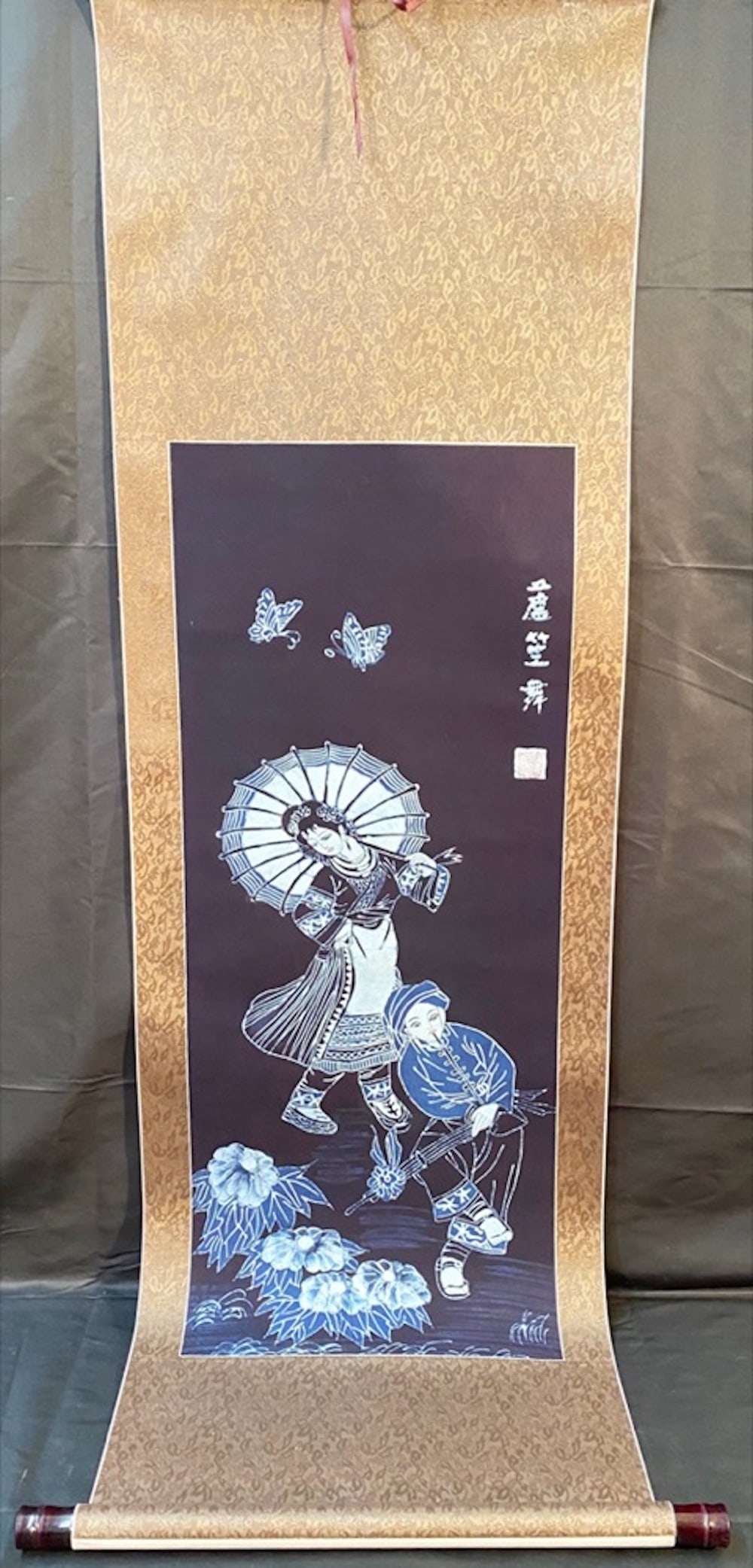 CHINESE SCROLL PAINTING ON A SILK BACKING ? 18 IN x 59 IN: A Chinese scroll painting depicting a woman dancing to a flute player with several butterflies. A beautiful painting, using dark blue paint, attached to a silk backing. It is signed in the upper right