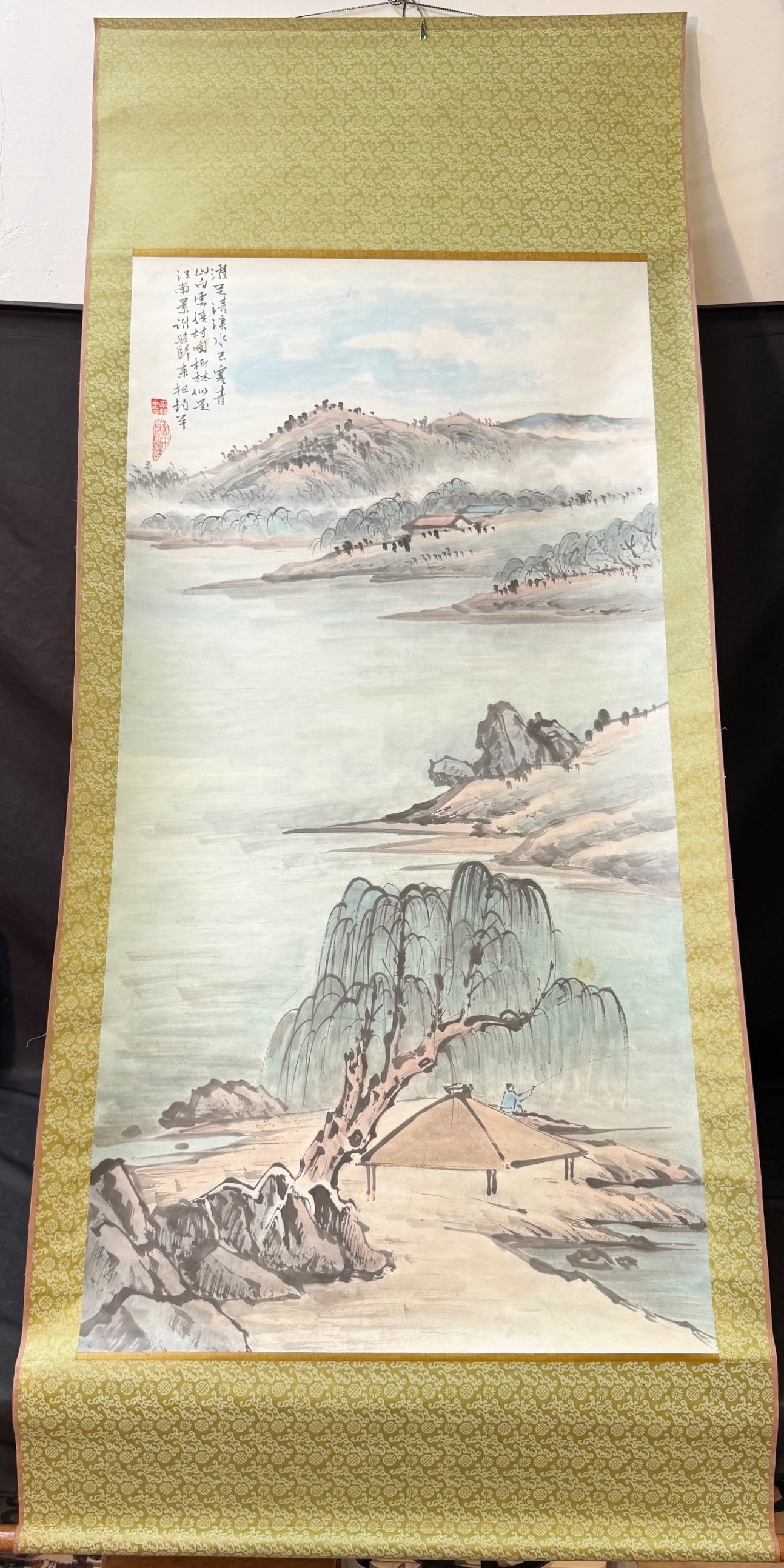 JAPANESE HANGING SCROLL PAINTING, 32IN x 76IN (81cm x 193cm): A refined Japanese hanging scroll depicting a?tranquil Jiangnan-style riverside landscape, rendered in ink with soft washes of light mineral color. In the foreground, a?thatched pavilion?rests beneath