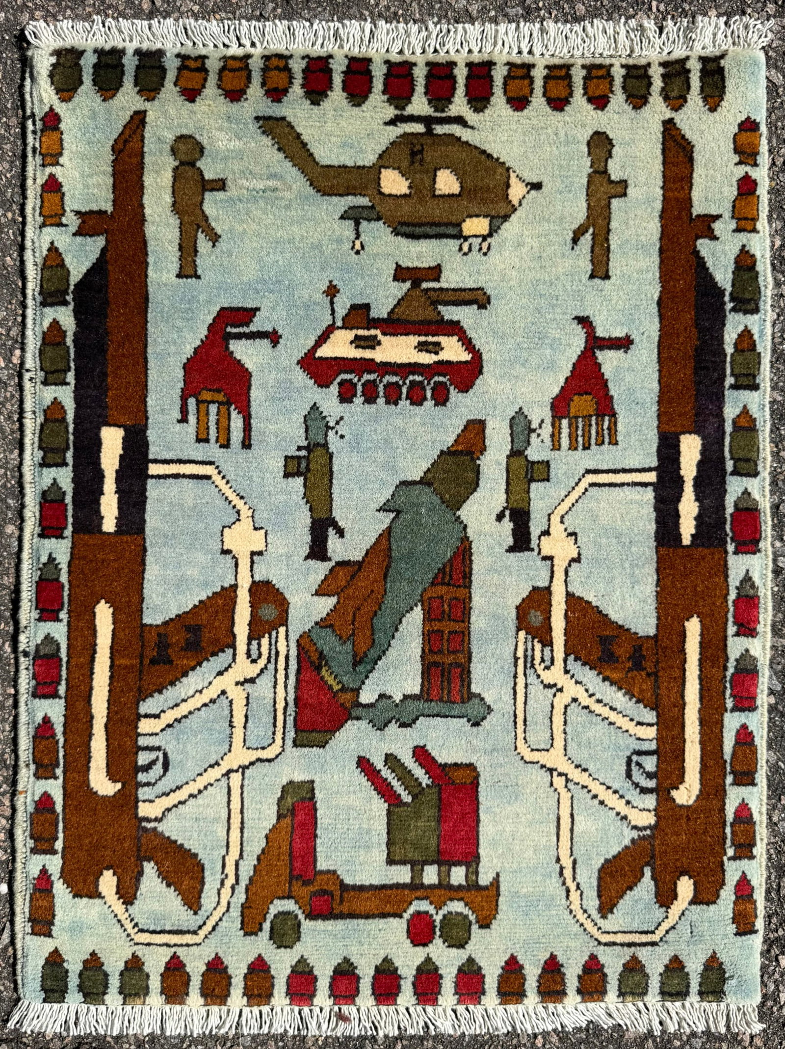 AFGHAN HAND KNOTTED WAR RUG WITH HELICOPTER, KALASHNIKOV, 2.0 x 2.6 (61cm x 76cm): An exceptional hand-knotted Afghan War Rug, masterfully woven in wool and featuring a visually compelling and within the war rug genre. Set against a dramatic light blue field, the design depicts a mi