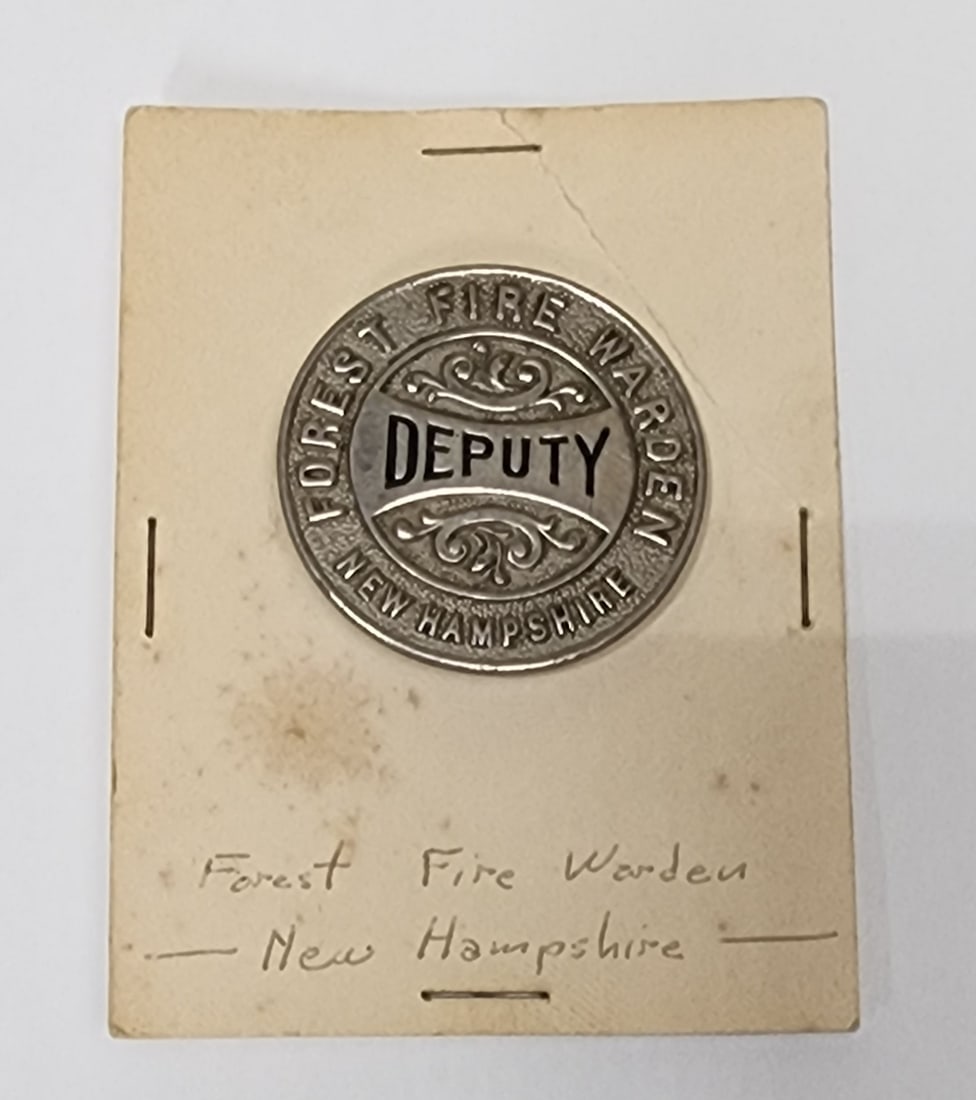New Hampshire Forest Fire Warden Badge: Early deputy forest fire warden badge from New Hampshire. This circular badge measures 1 3/4" in diameter. It has the original pinback and catch on the back. This badge was made by Boston Badge Compan