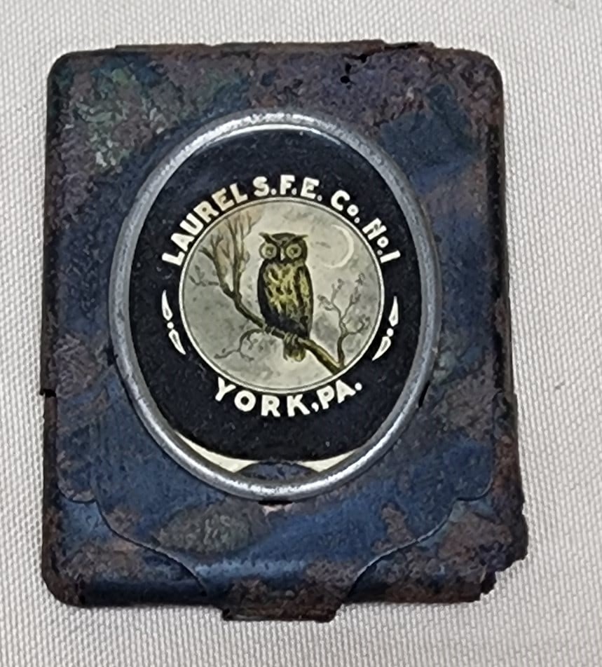 Laurel Fire Company York Pa Match Safe: A metal match safe from the Laurel Fire Company of York PA. The safe features the Laurel owl on a celluloid insert. It measures 2" by 2 3/4". It is rough condition as the metal is quite rusted.