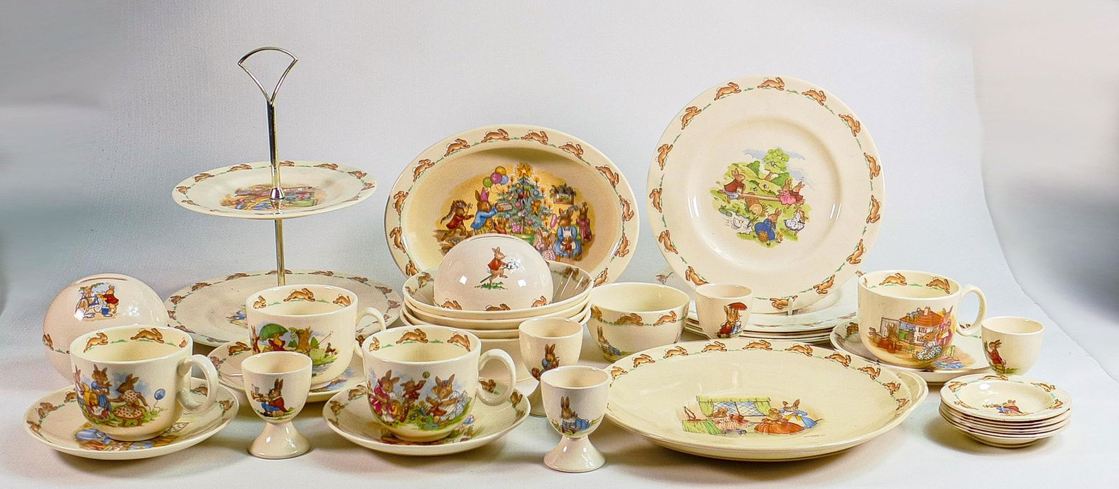 Royal Doulton Bunnykins items to include - cup & saucer sets, bowls, money boxes, egg cups & a two: Royal Doulton Bunnykins items to include - cup & saucer sets, bowls, money boxes, egg cups & a two tier cake stand etc.