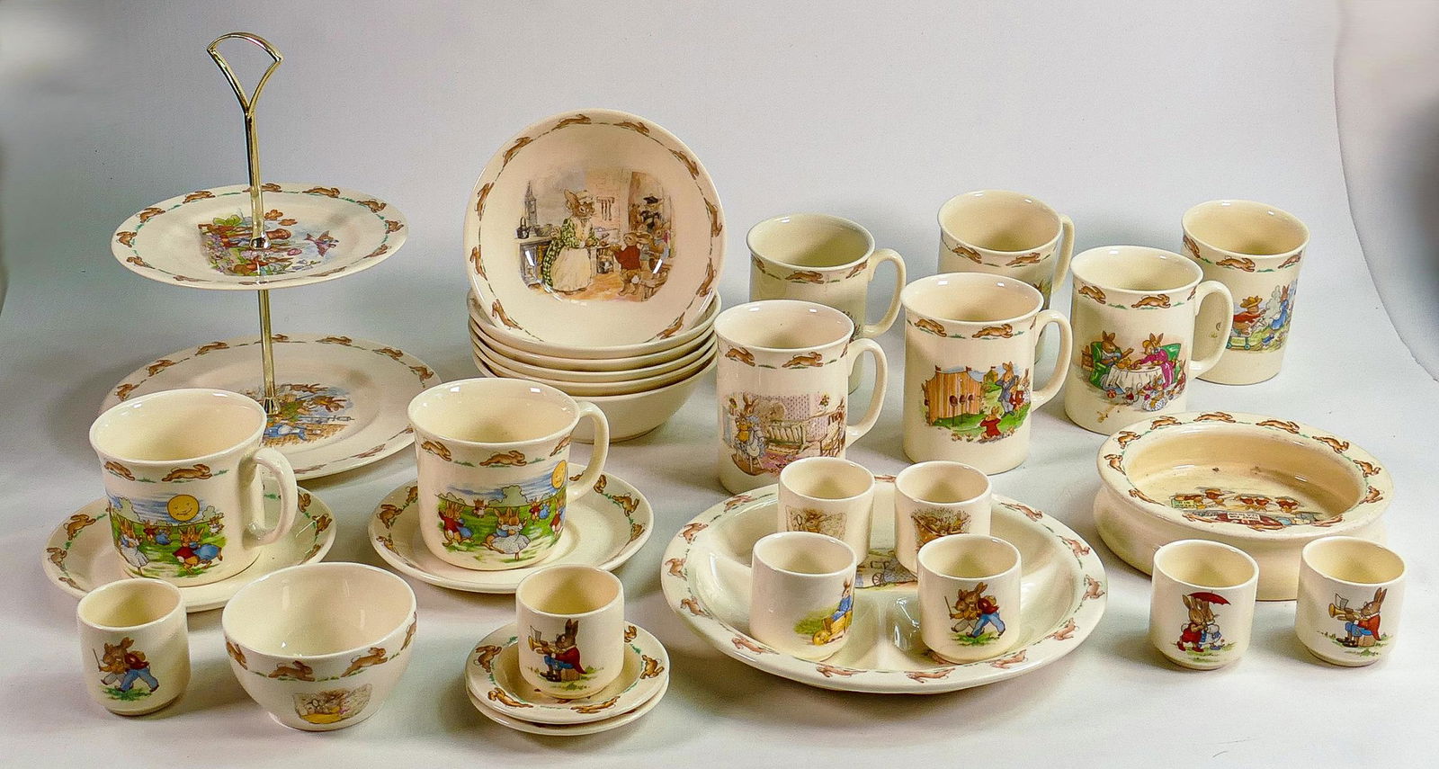 Royal Doulton Bunnykins items to include - cups and saucers, oatmeal dishes, bowls, egg cups, mugs &: Royal Doulton Bunnykins items to include - cups and saucers, oatmeal dishes, bowls, egg cups, mugs & two tier cake stand.