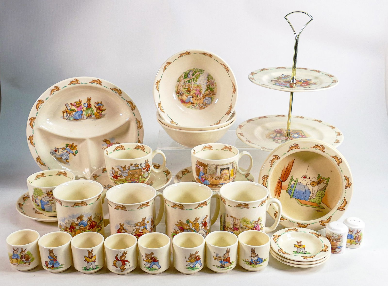 Royal Doulton Bunnykins items to include - cups and saucers, oatmeal dishes, bowls, egg cups, mugs &: Royal Doulton Bunnykins items to include - cups and saucers, oatmeal dishes, bowls, egg cups, mugs & two tier cake stand.