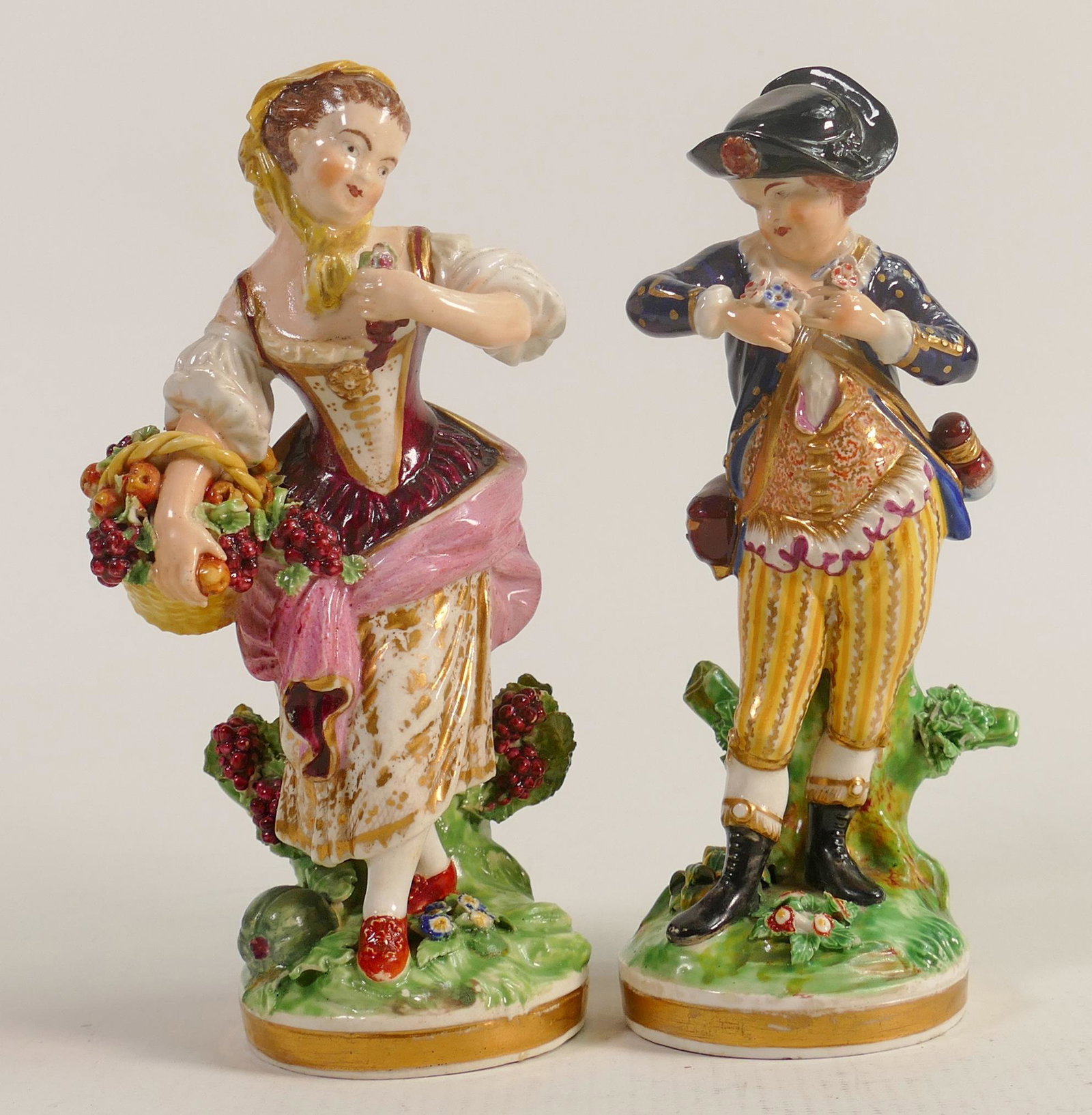 A pair of continental figures in the style of Meissen. Lady with fruit basket and a boy with: A pair of continental figures in the style of Meissen. Lady with fruit basket and a boy with flowers. Petal and leaf damage, lady's shoulders and neck has been restored.