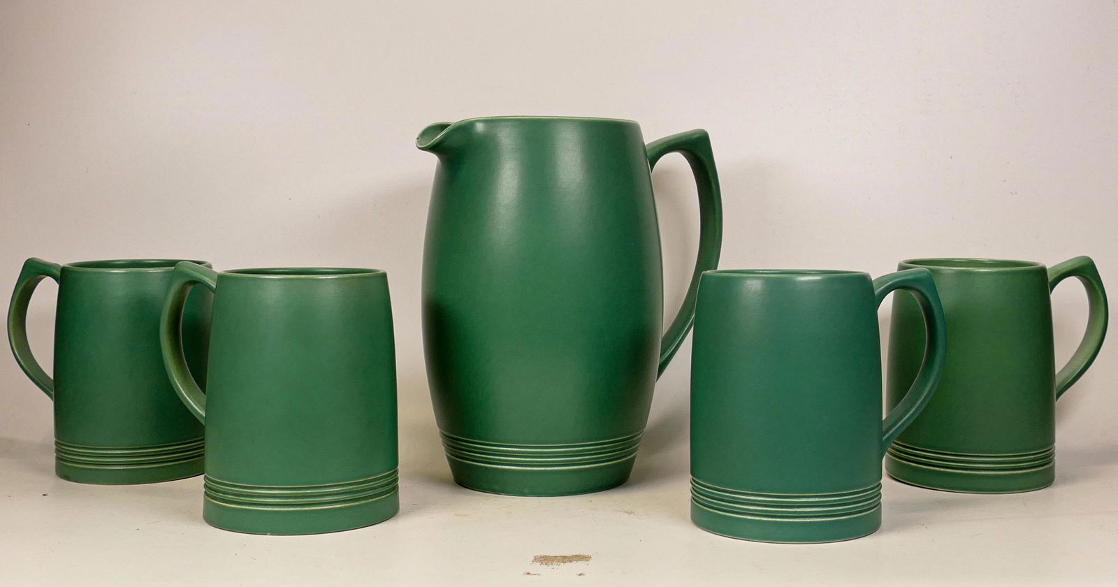 Wedgwood Keith Murray water jug & tankards in matt green glaze, 1 tankard nibbles to base rim,: Wedgwood Keith Murray water jug & tankards in matt green glaze, 1 tankard nibbles to base rim, height of tallest 20cm (5)