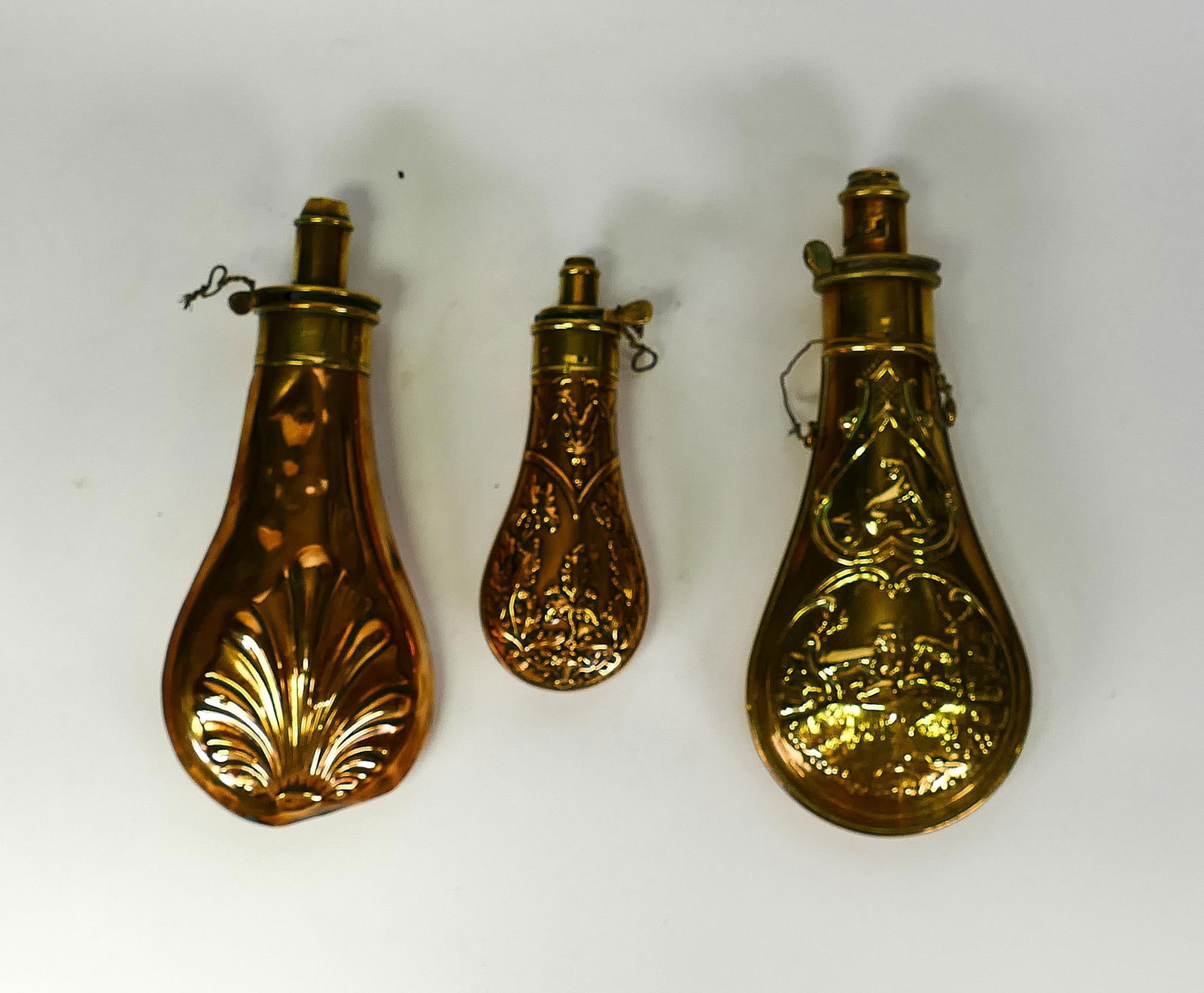 Three 19th century embossed copper and brass powder flasks, two by G.& J.W. Hawksley & signed to the: Three 19th century embossed copper and brass powder flasks, two by G.& J.W. Hawksley & signed to the spout, together with similar, tallest 19.5cm(3)