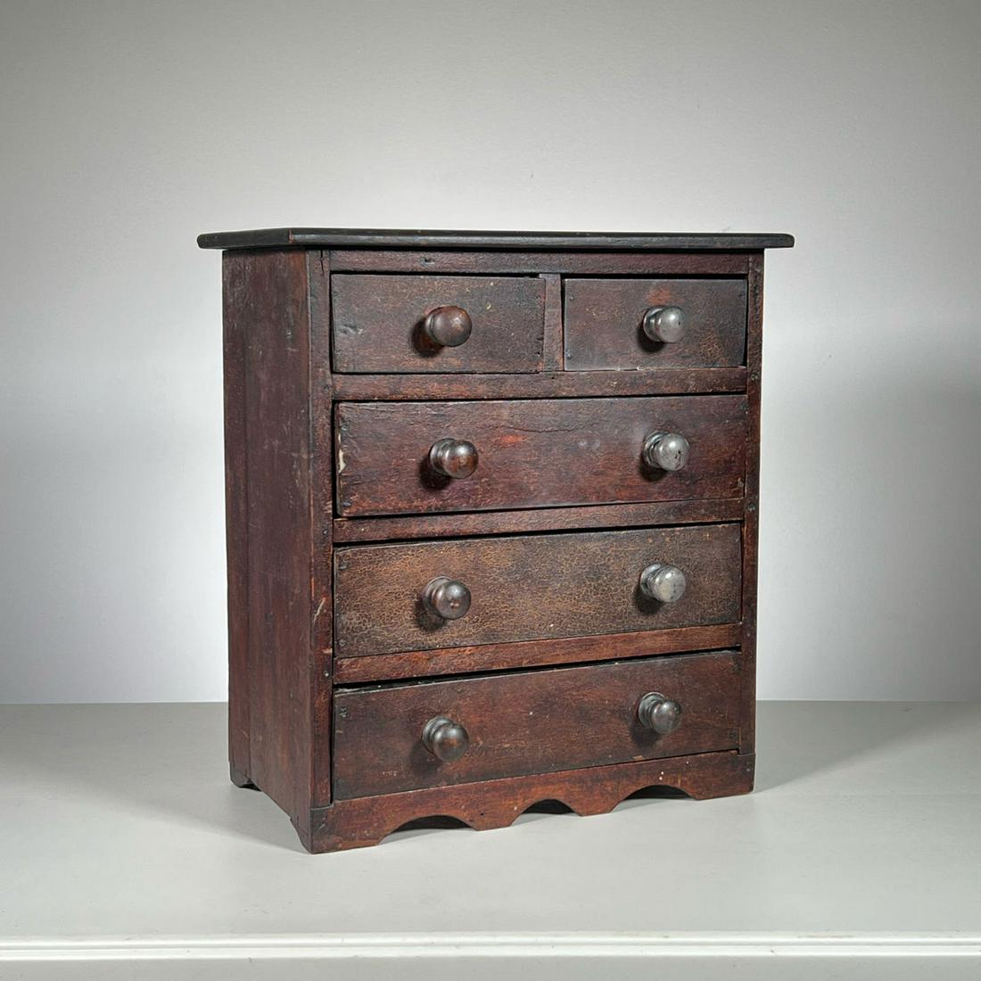 MINIATURE DOVETAILED CHEST: Chest in old dark finish, crackled and worn. Two drawers over four with wood knobs. Inventory Code: 1K-174 Provenance: Part of over six-hundred Items consigned from an important Millwood, NY family