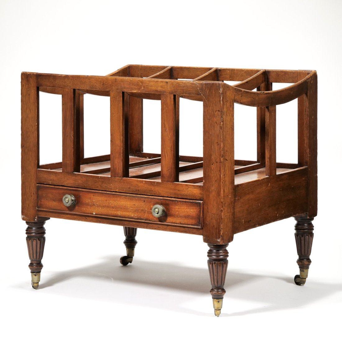 ANTIQUE WOOD CANTERBURY: Having four equal partitions with curved top over a full width drawer with round brass pulls and cockbeading, raised on turned and fluted legs with brass casters - l. 21 x w. 16.25 x h. 19.5 in. Prove