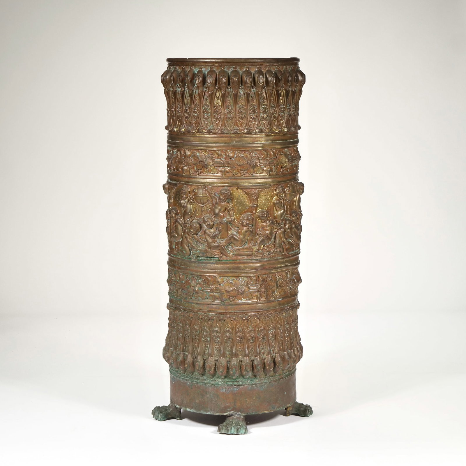 ORNATE BRASS STICK HOLDER/ UMBRELLA STAND: With repousse decoration of foliage patterns and putti between scenes separated by columns, raised on claw feet - h. 23 x dia. 8.5 in. Provenance: Johanna Ransohoff (1907-); descended through the fami
