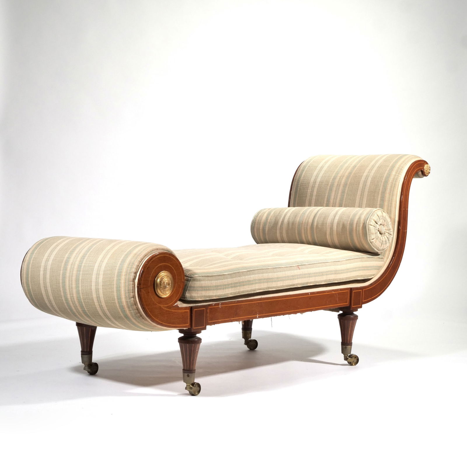 A FINE GEORGIAN SCROLL CHAISE LOUNGE C. 1810-1820: or daybed; having very fine line inlay throughout, turned legs with line inlay raised on oversized brass casters, and gilt carved lion and ring mounts and gilt rosettes h. 32.5 x w. 24 x l. 68 in. Pro
