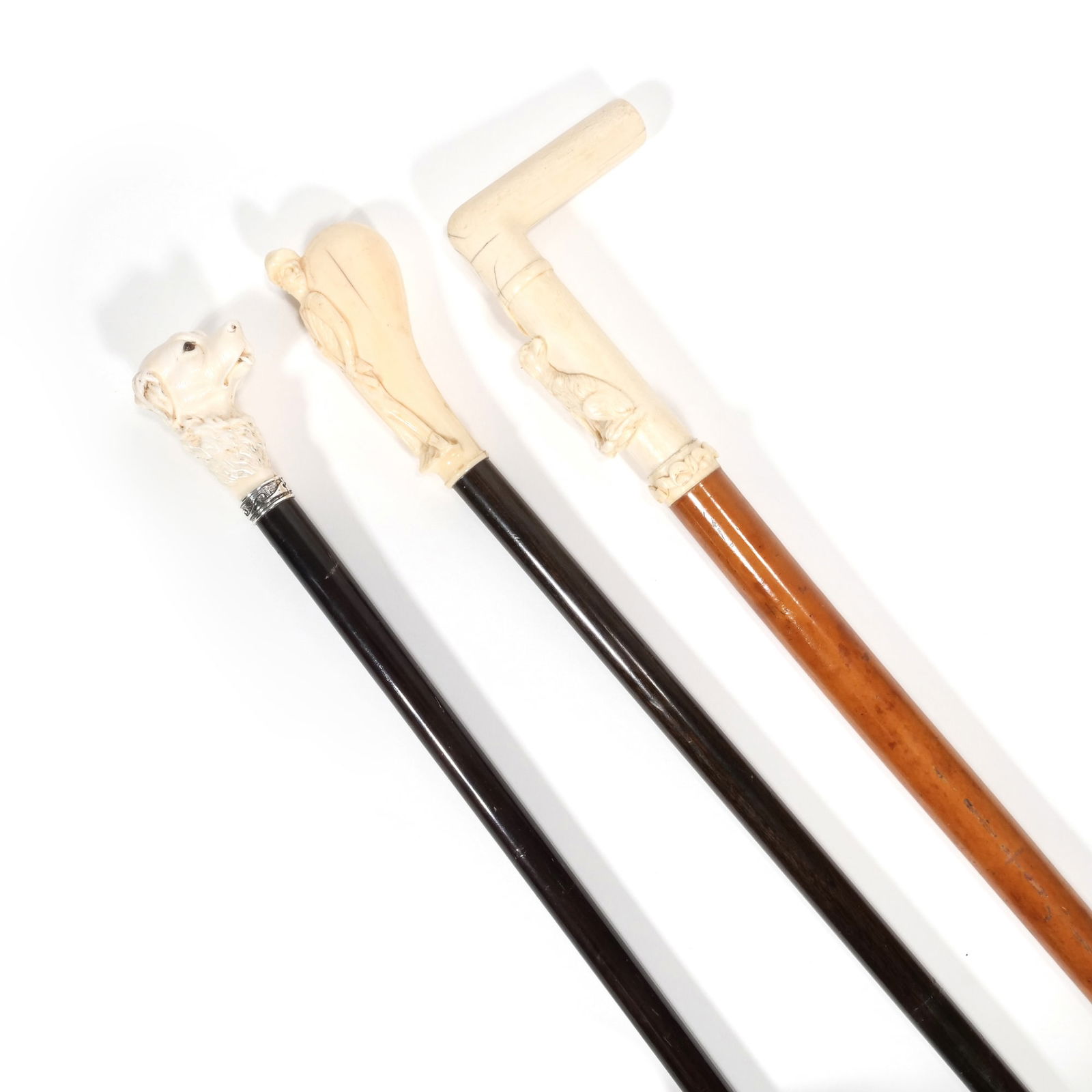 (3pc) ANTIQUE ENGLISH CARVED BONE HANDLED WALKING STICKS: Including, one carved dogs head cane with glass bead eyes and a silver collar and rosewood shaft, one with a rounded grip and carved figure of a boy holding a rifle with a rosewood shaft,&nbsp; pl