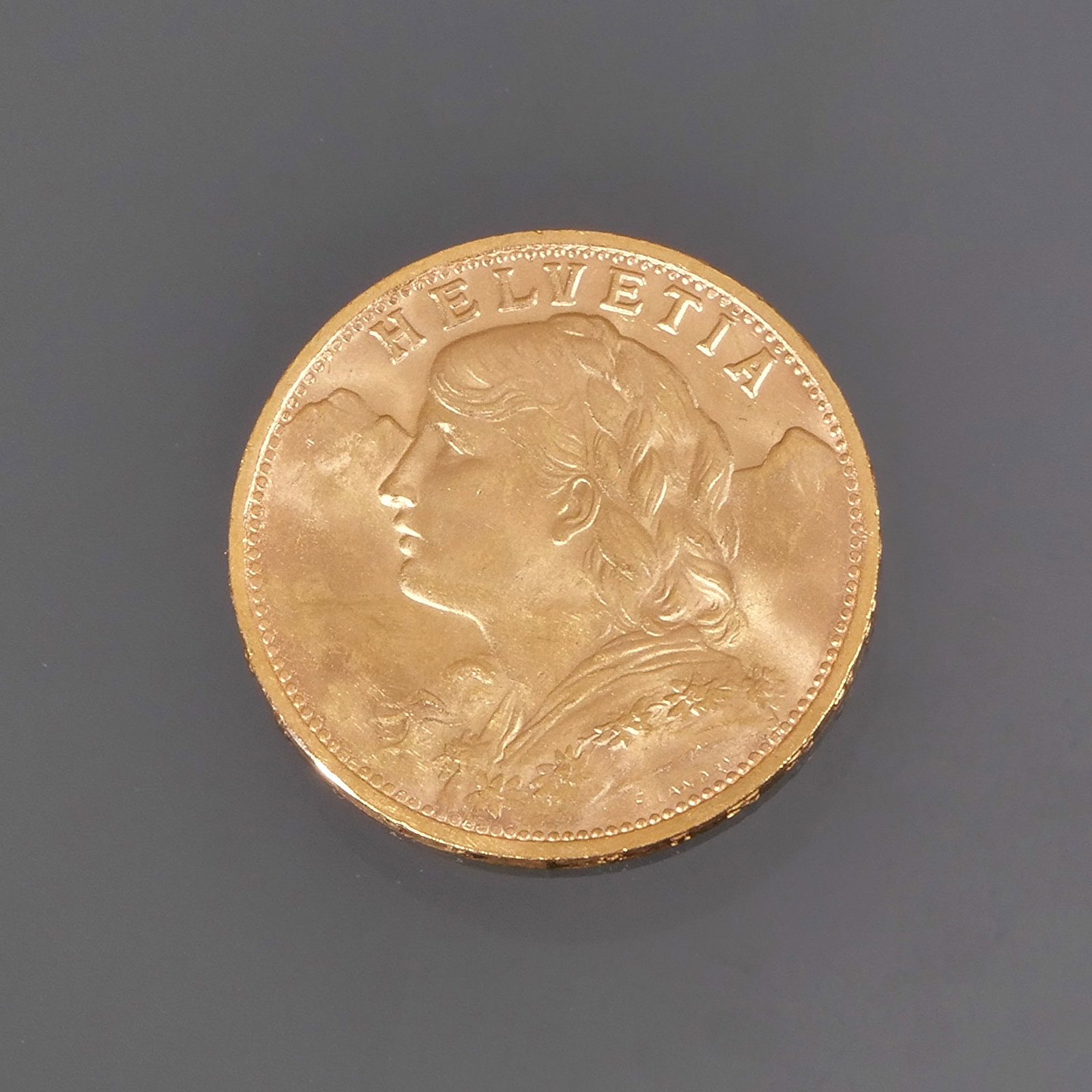GOLD SWISS 'HELVETIA' COIN: A 1947 Swiss 20 Franc gold coin (vreneli), the obverse featuring the allegorical female figure of "Helvetia", and the reverse depicting the Swiss shield with the Swiss Cross, surrounded by oak leaves,