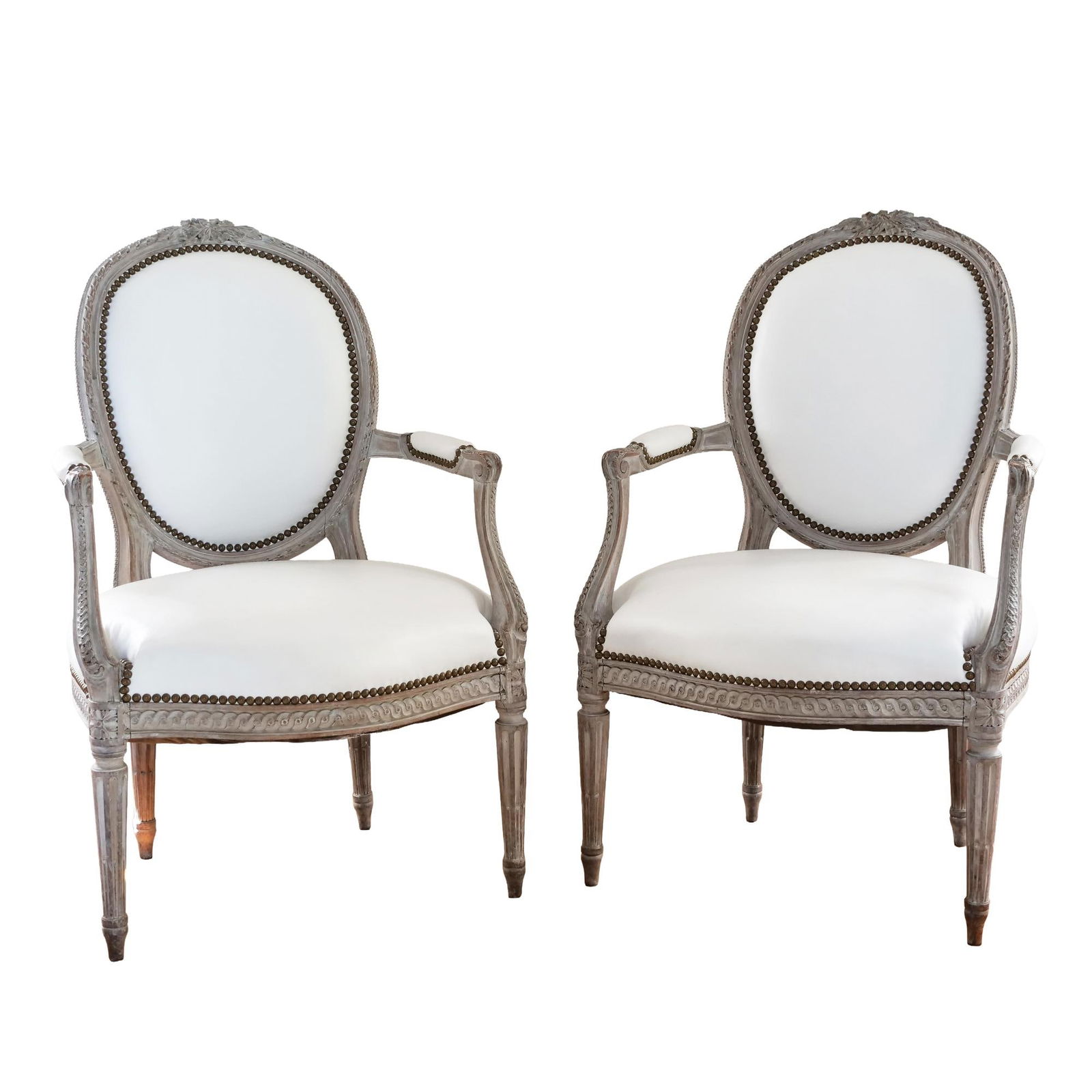 PAIR LOUIS XVI CARVED FAUTEUILS, WHITE LEATHER: Pair of oval-back armchairs (fauteuils) in Louis XVI style. Carved wood frames with a graywashed finish. Oval medallion backs and seats padded and upholstered in white leather. Single row of round met