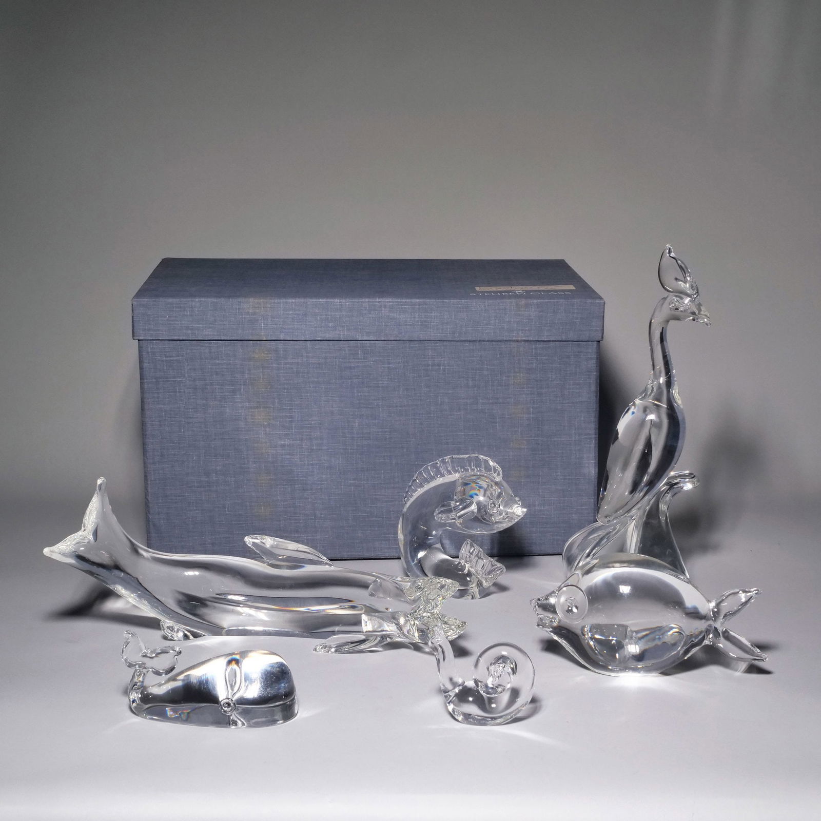 (6pc) STEUBEN GLASS ANIMAL FIGURINES, INCL. LLOYD ATKINS PHOENIX: A group of Steuben crystal glass animal sculptures, including a Lloyd Atkins designed phoenix (h. 13.5 in.), a kissing fish (h. 4.5 in.), a leaping fish (h. 5.5 in.), a long trout (6 in.), a whale, an