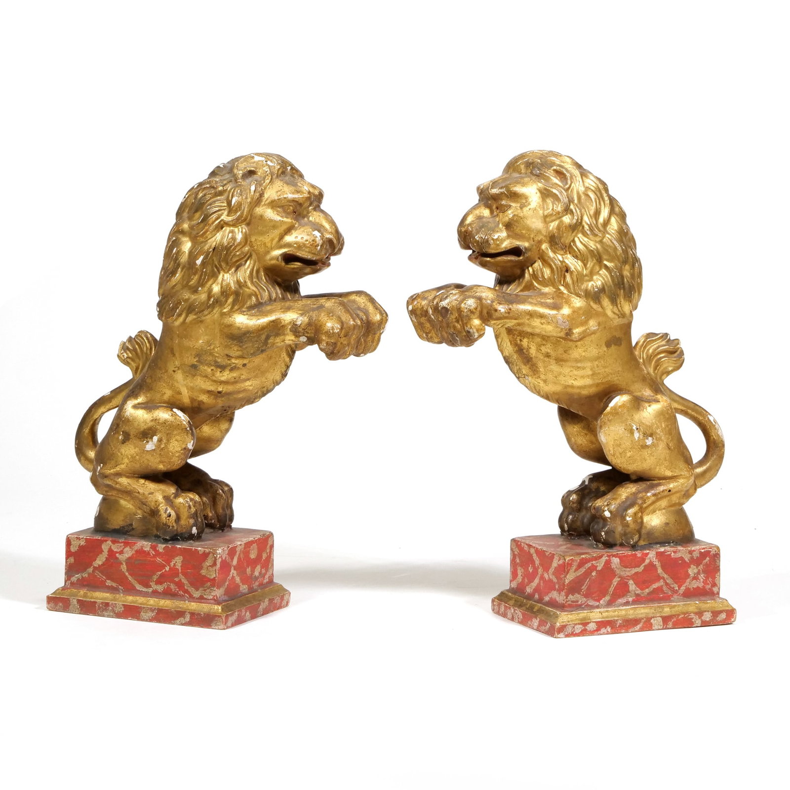 18TH/19TH C. GILTWOOD LIONS SALIENT ORNAMENTAL FIGURES: Pair of Lions Salient Giltwood and gesso on painted wood bases Carved wood figures in a salient pose with a gilt finish over a gesso ground, mounted on red and gold marbled plinths. - h. 12 x w. 3.5 x