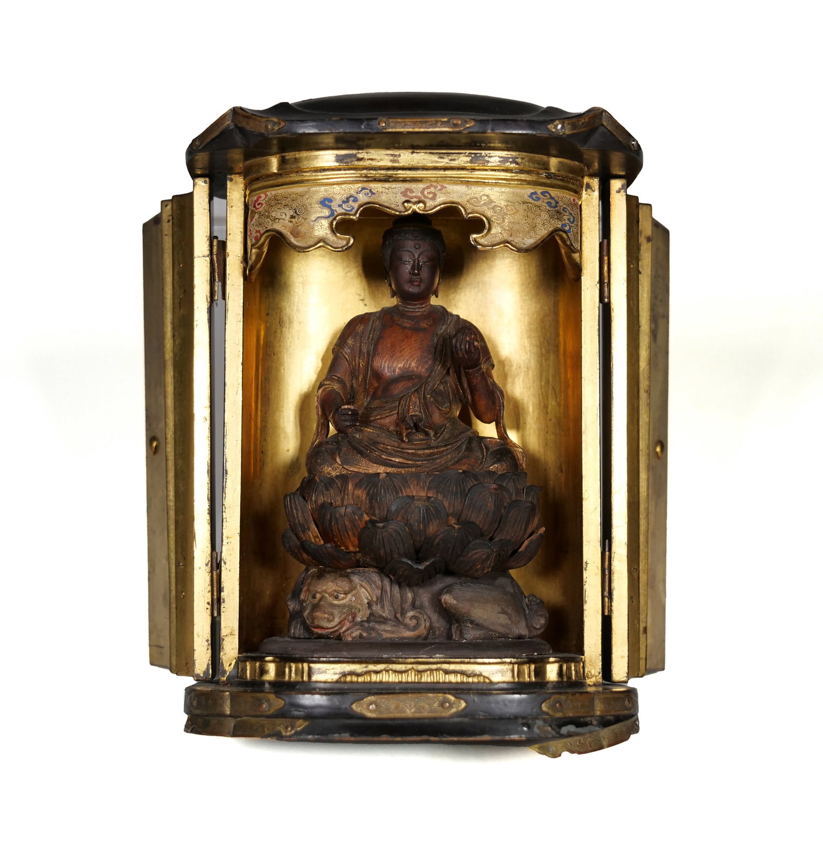 JAPANESE LACQUERED WOOD ZUSHI SHRINE WITH SEATED DEITY, BUDDHA: The portable shrine features a black lacquered exterior with chased metal hardware and a double-door opening. The gilded interior houses a hand-carved wooden figure seated upon a tiered lotus throne