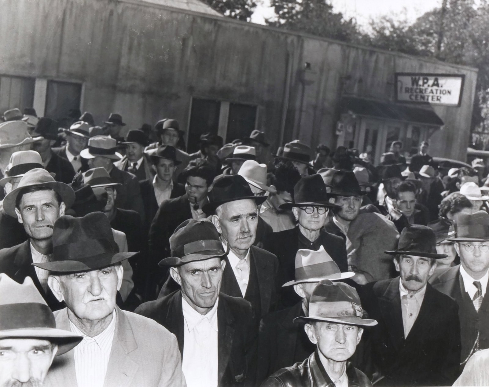 THEODORE FONVILLE WINANS (AMERICAN, 1911-1992): Long Watchers 15.25 x 19 in. (sight) Photograph depicting men standing outside the W.P.A. Recreation Center - h. 20.25 x w. 24.25 in. (frame) Inventory No. 64-19 Provenance: Accompanied by a document 