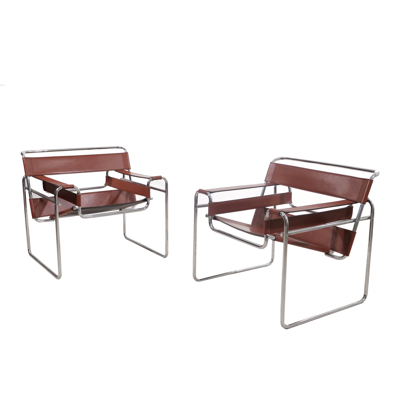 PAIR OF MILO BAUGHMAN STYLE CHROME AND LEATHER SLING ARMCHAIRS: Each armchair features a tubular chrome-plated steel frame with brown leather sling panels for the seat, backrest, and armrests. The leather components are detailed with tonal stitching and the frame 