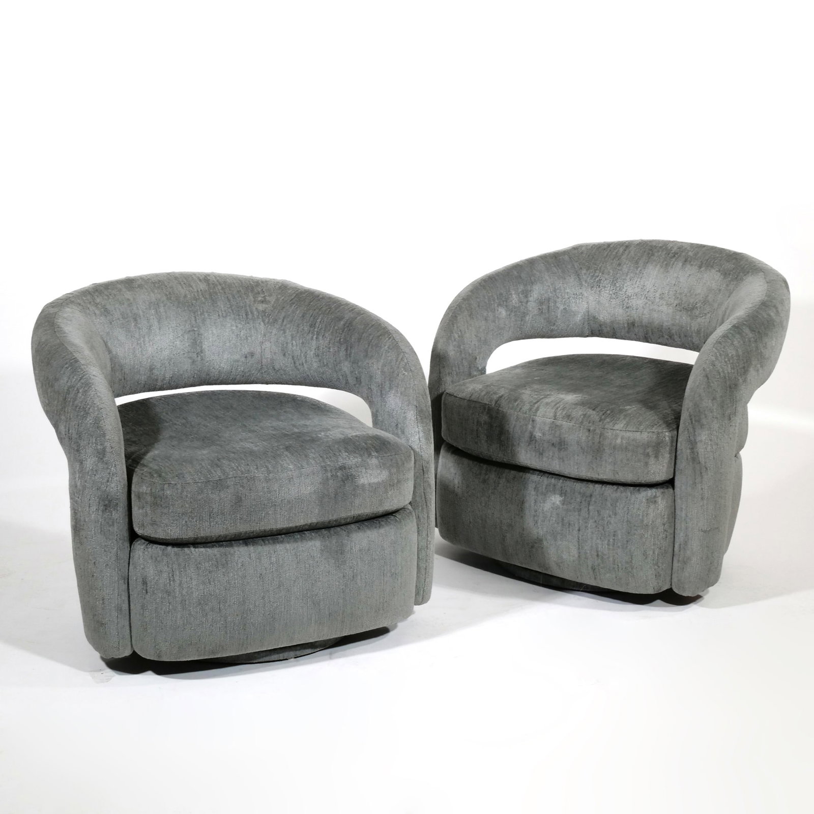 PAIR INTERLUDE HOME SWIVEL ARMCHAIRS: Pair of barrel-back swivel armchairs upholstered in a textured grey fabric with horizontal backrest opening, each with a seat height of 18 inches. Built on fully upholstered bases with swivel