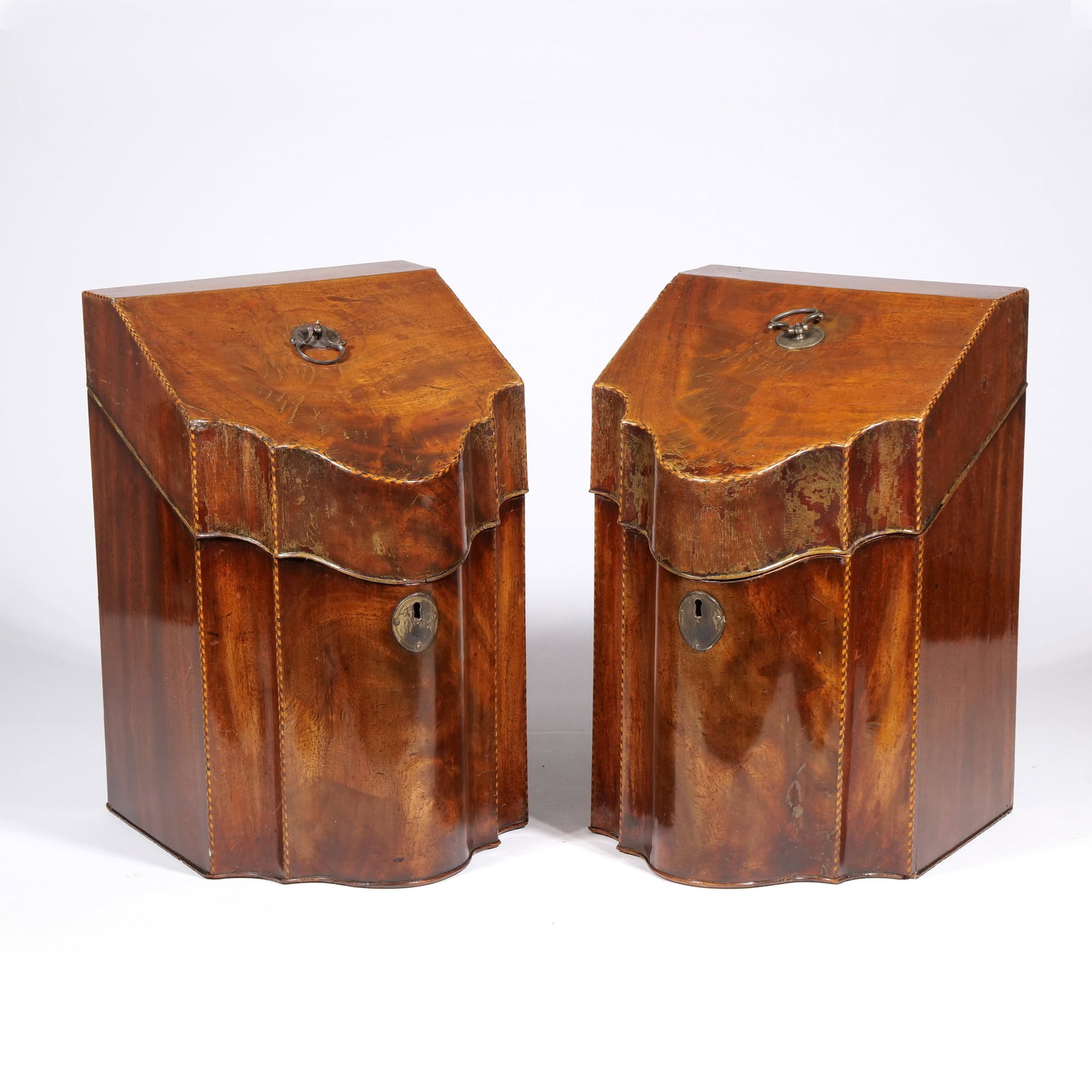 (2pc) PAIR OF GEORGE III STYLE MAHOGANY SERPENTINE KNIFE BOXES: Each box features a serpentine front and a sloping lid veneered in mahogany with decorative chevron stringing. The interiors contain tiered cutlery dividers and an inlaid star on the underside of