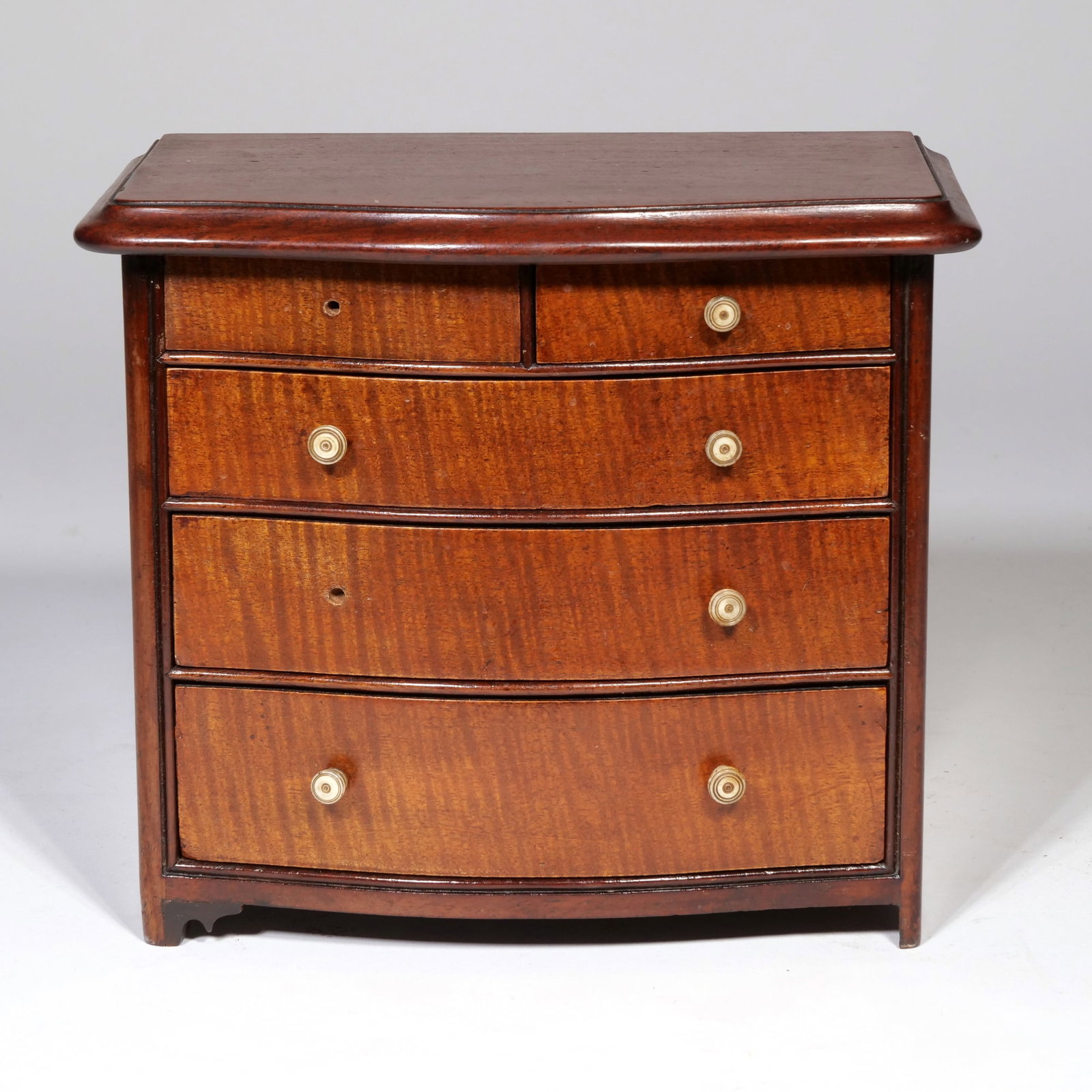 FEDERAL STYLE MINIATURE TIGER MAPLE BOWFRONT CHEST OF DRAWERS OR SALESMAN'S SAMPLE: This miniature bowfront chest features two small top drawers over three graduated full-width drawers with tiger maple veneer fronts. The carcass and molded top are constructed from a dark-stained