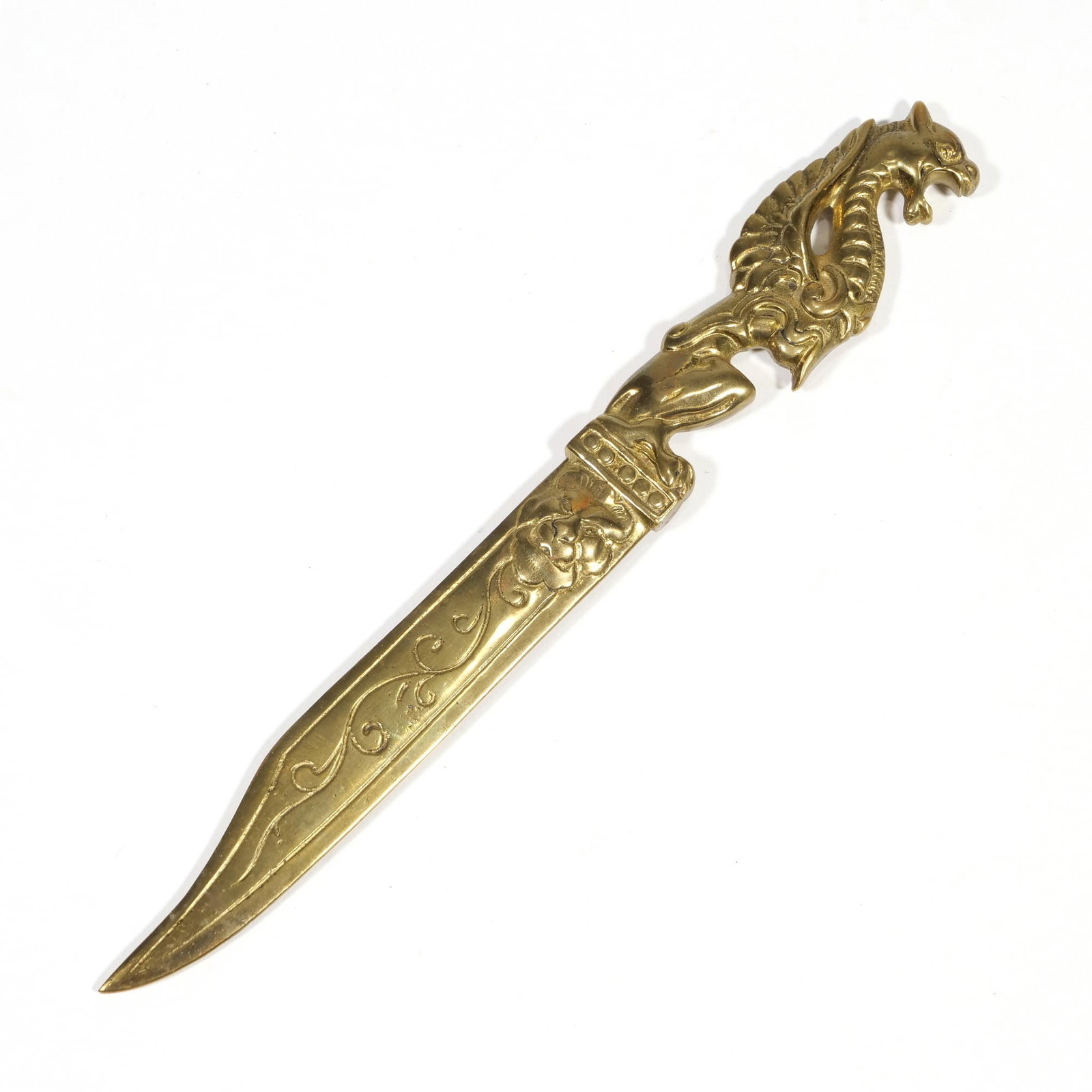 CAST BRASS DRAGON-HANDLED LETTER OPENER: Cast brass letter opener featuring a hilt in the form of a winged dragon. The blade is decorated with an embossed mythological mask at the bolster and scrolled vine patterns along the length. Both sid
