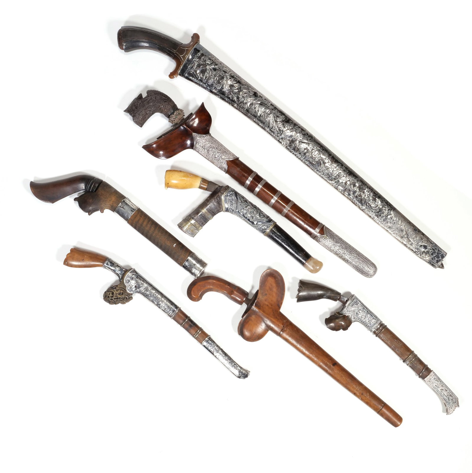 (7pc) SOUTHEAST ASIAN SWORDS & DAGGERS: A collection of swords and daggers including a decorative sabre (likely a kilij or shamshir) with intricate silver tone scabbard and carved handle (longest), a traditional Indonesian dagger (keris or