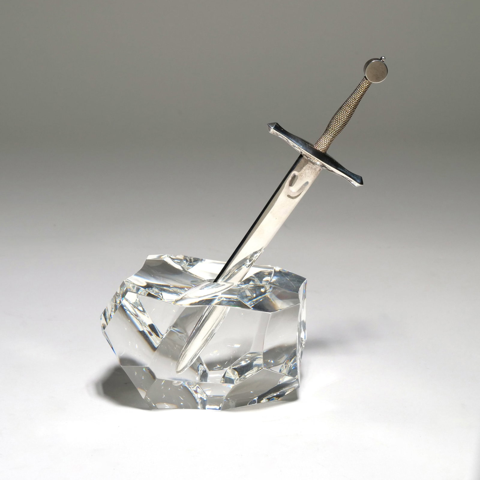 STEUBEN / JAMES HOUSTON GLASS "EXCALIBUR" CRYSTAL, STERLING SILVER, AND 18K GOLD LETTER OPENER: By James Houston for Steuben, designed as a faceted crystal rock-form base and a removable sterling silver sword-form letter opener with 18k gold accents on the hilt. The crystal base is etched with t