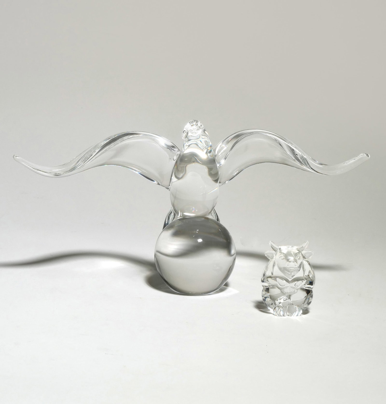 (2pc) STEUBEN CRYSTAL EAGLE ON GLOBE AND BULL FIGURINES: The set comprises a large clear crystal eagle with outstretched wings perched atop a spherical base and a smaller stylized bull figurine. The eagle measures 13 inches in width and 6.5 inches in height