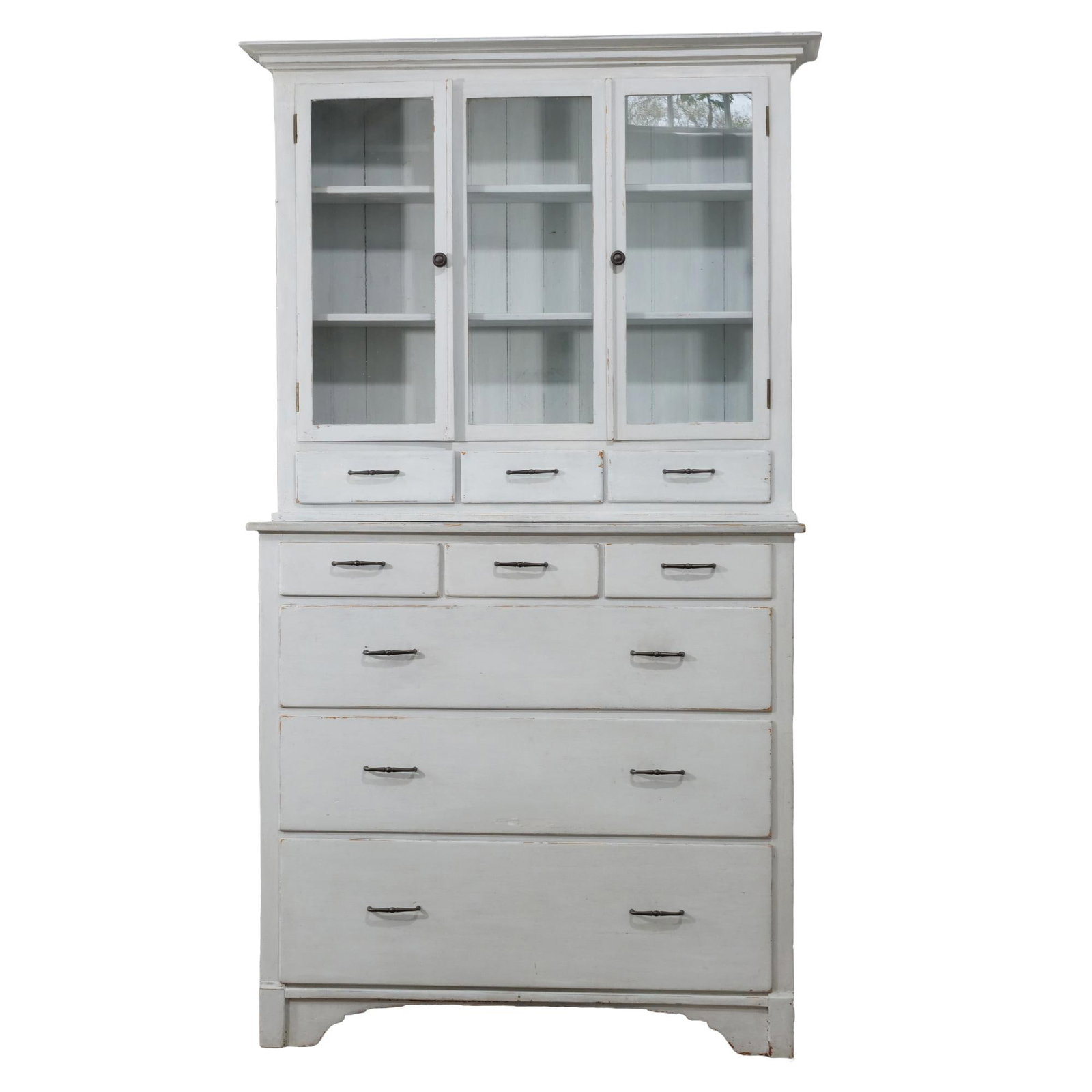 19TH CENTURY CANADIAN STEPBACK WHITEWASHED PINE CHINA CABINET: This two-piece wooden cabinet features a whitewashed finish and dark metal pull hardware. The upper section contains three glass-paneled doors enclosing shelves above three small drawers. The lower ba