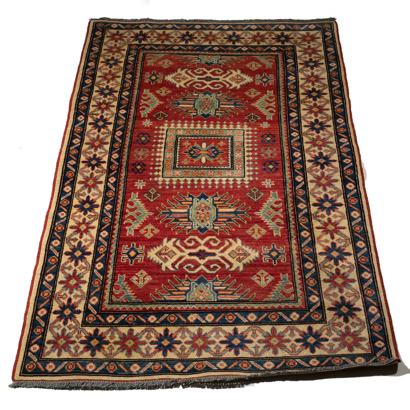KAZAK HAND-KNOTTED WOOL RUG: This hand-knotted wool rug features a saturated red field decorated with three primary geometric medallions and various smaller motifs. The design incorporates a palette of indigo blue, cream, and