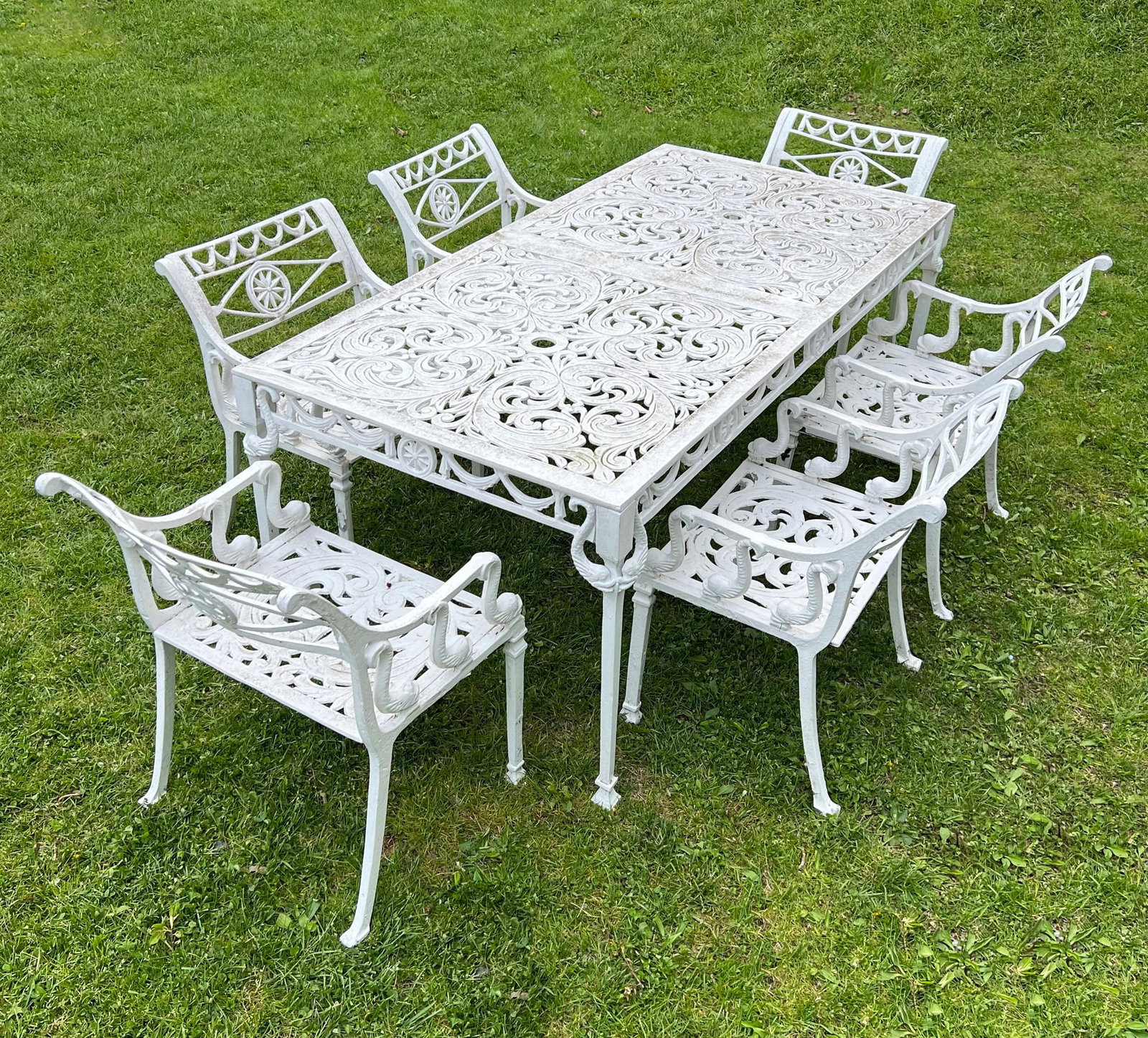 (7pc) REGENCY-STYLE CAST ALUMINUM GARDEN DINING SET WITH SWAN MOTIF: Outdoor dining suite comprising a rectangular table and six matching armchairs, all featuring intricate pierced scrolling foliate and acanthus leaf patterns in a white painted finish. The chair armres