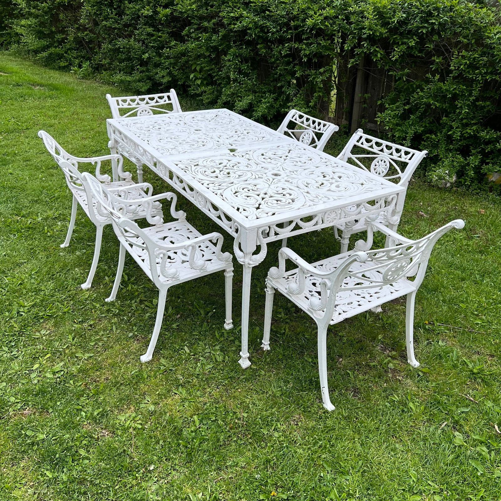 (7pc) REGENCY-STYLE CAST ALUMINUM GARDEN DINING SET WITH SWAN MOTIF: Outdoor dining suite comprising a rectangular table and six matching armchairs, all featuring intricate pierced scrolling foliate and acanthus leaf patterns in a white painted finish. The chair armres
