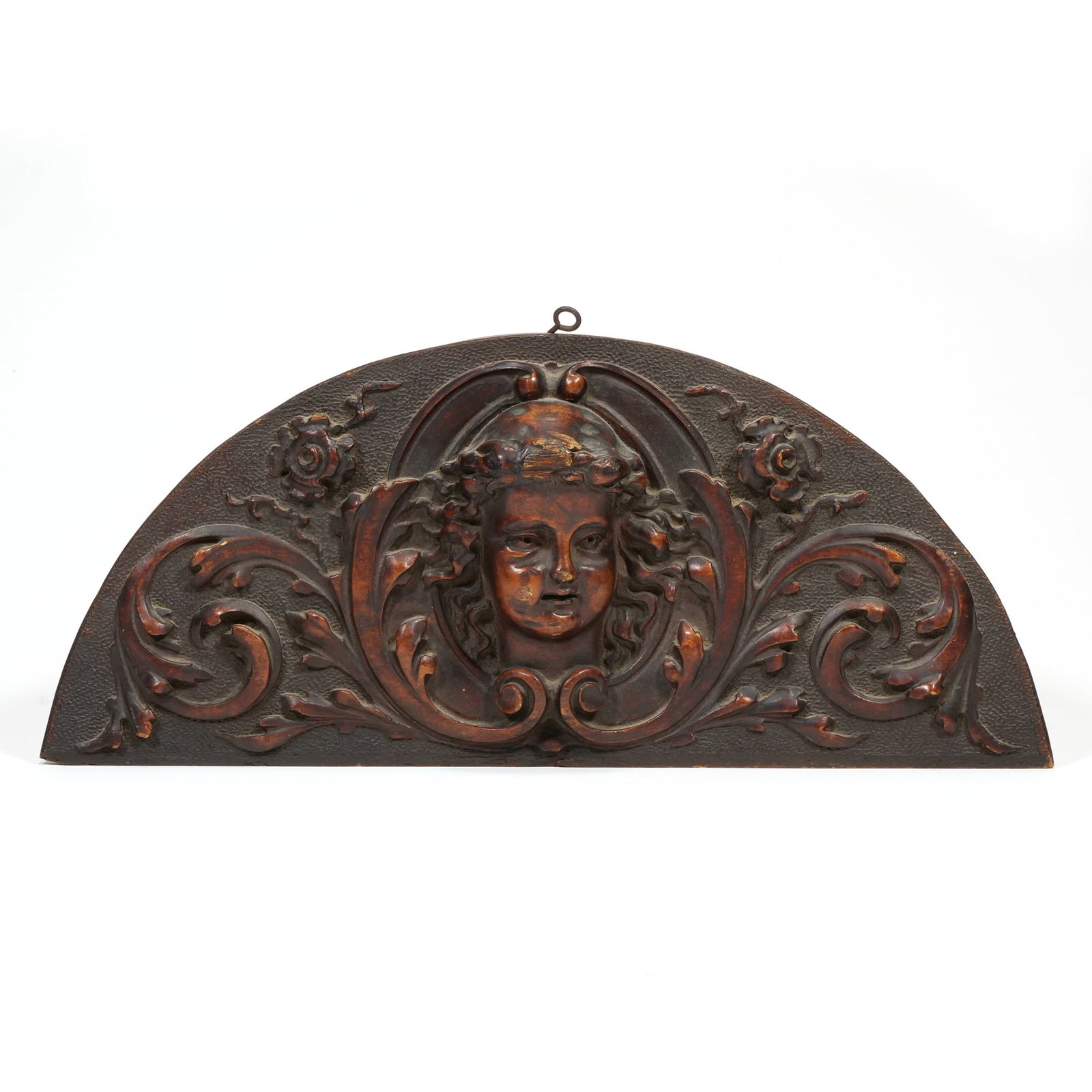 ITALIAN RENAISSANCE REVIVAL CARVED WOOD CHERUB LUNETTE: Carved dark-stained wood lunette featuring a central high-relief cherub head. The figure is flanked by symmetrical acanthus leaf scrolls and floral rosettes against a textured background. A metal hang
