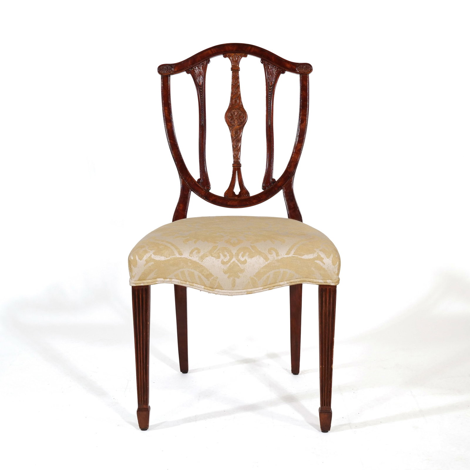 GEORGE III STYLE CARVED MAHOGANY SHIELD-BACK SIDE CHAIR: Featuring a mahogany shield-back frame with a central splat decorated with an intricately carved floral rosette and braided motifs. Two flanking splats contain carved beaded detailing, supported by ta
