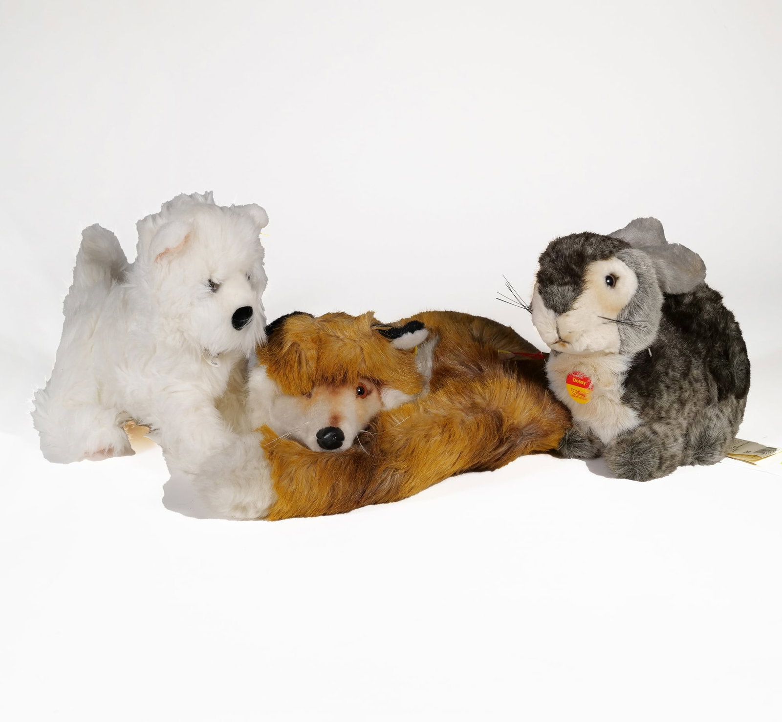 (3pc) STEIFF PLUSH ANIMAL LOT: DOSSY RABBIT, FUZZY FOX, AND SAM TERRIER: This lot features three Steiff plush animals including a reclining fox, a seated rabbit, and a standing white terrier. Each piece retains its original circular chest tag identifying them as Fuzzy,