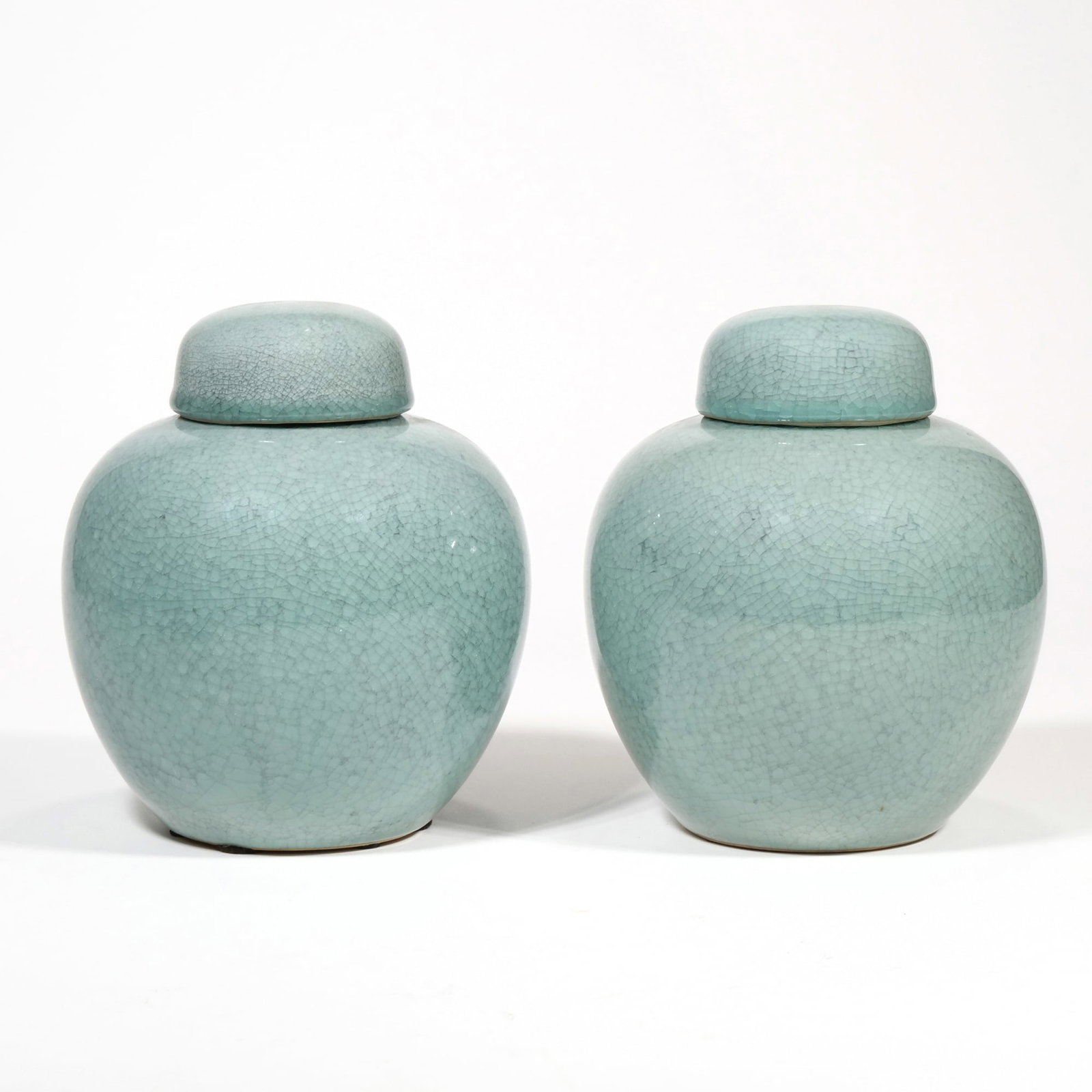 PAIR OF CHINESE CELADON CRACKLE GLAZE LIDDED JARS, GUAN-WARE: A pair of bulbous porcelain jars finished in a light celadon glaze with an all-over fine crackle pattern. Each jar features a matching domed lid and an unglazed foot rim. The set includes two