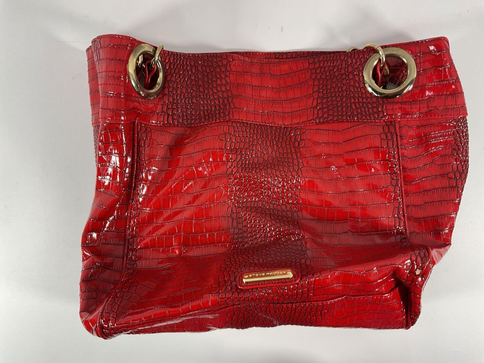Steve Madden Red Crocodile-Embossed Tote Bag: This is a Steve Madden red crocodile-embossed tote bag , featuring a glossy faux leather finish with an alligator skin pattern. The bag has a structured, oversized design , making it a statement piece