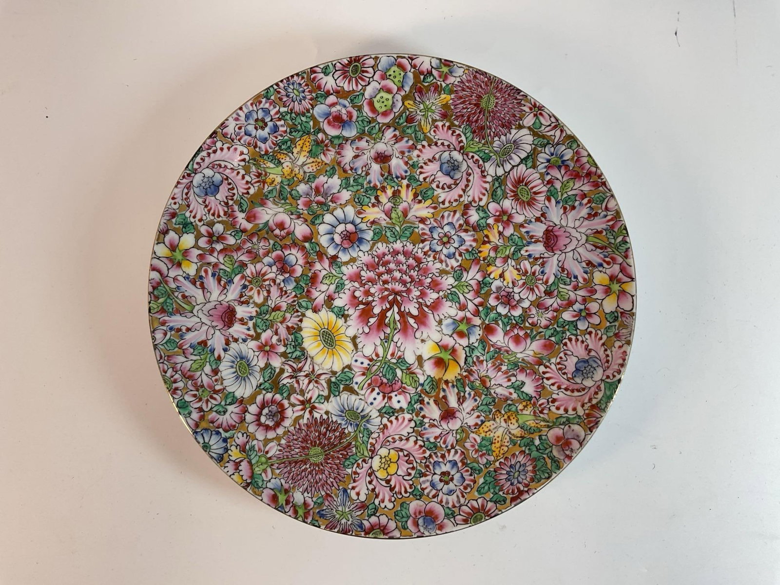 Chinese Porcelain Floral Plate - Hong Kong: This is a vintage Chinese porcelain plate featuring a densely detailed floral millefleur (thousand flowers) pattern. The plate is adorned with vibrant chrysanthemums, peonies, and other blossoms in pi