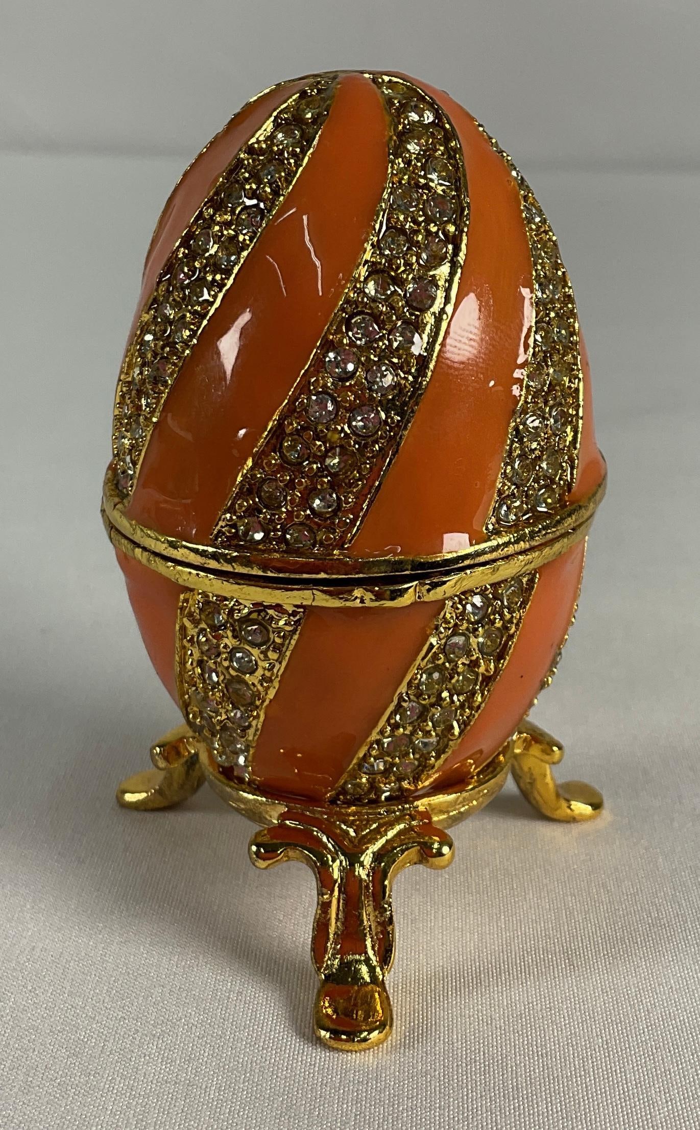 Decorative Egg, Faberge Style - Sherbert: A delicately crafted box shaped like an egg, adorned with a whimsical jewels. The egg rests on an ornate gold-tone stand with intricate detailing. Painted in a combination of white and gold with soft