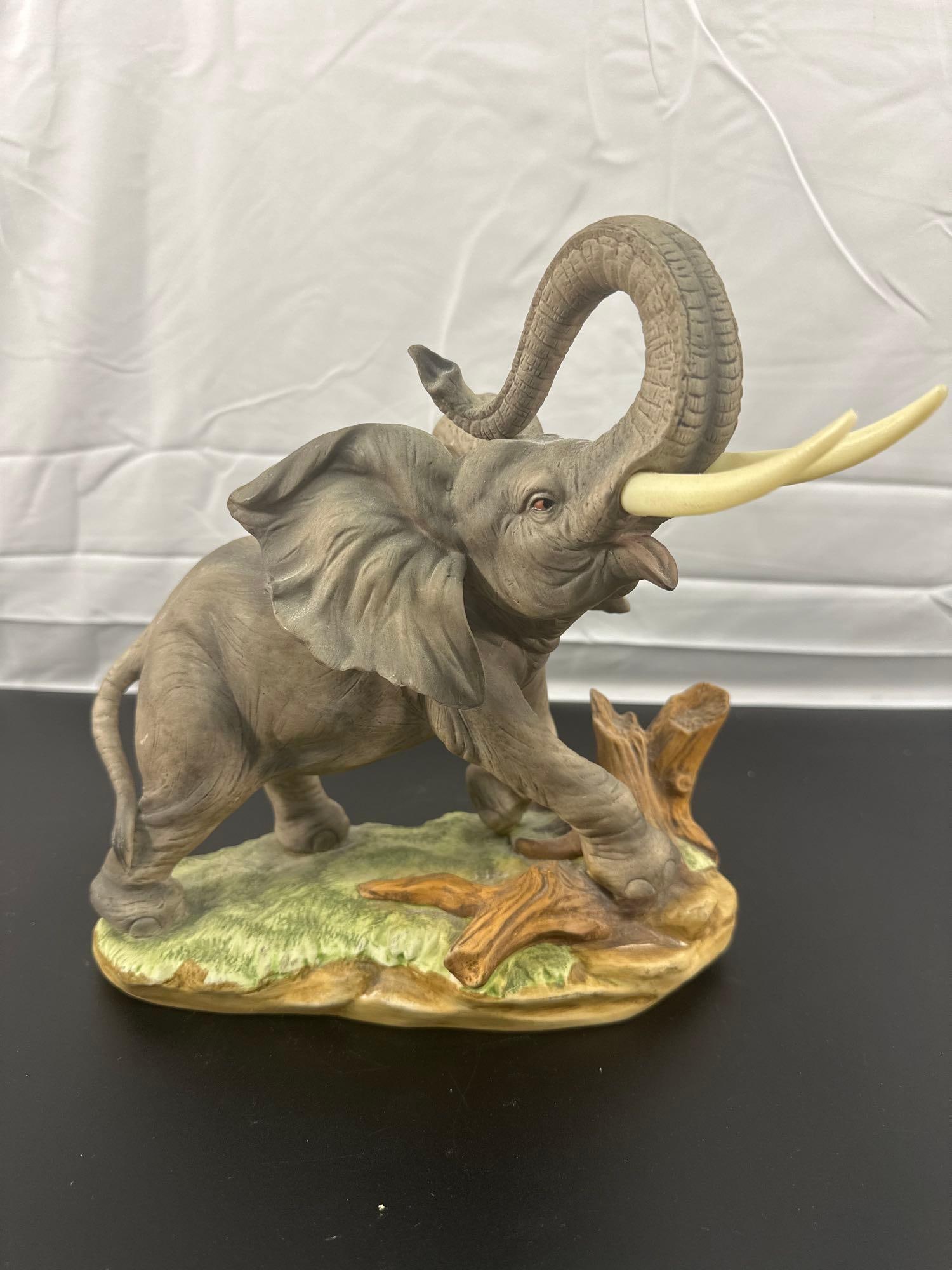 Left on China Porcelain Elephant Figurine KW5060: This figurine is a finely detailed porcelain sculpture of an elephant with its trunk raised, symbolizing good luck. The piece captures a dynamic pose with the elephant stepping over a naturalistic bas