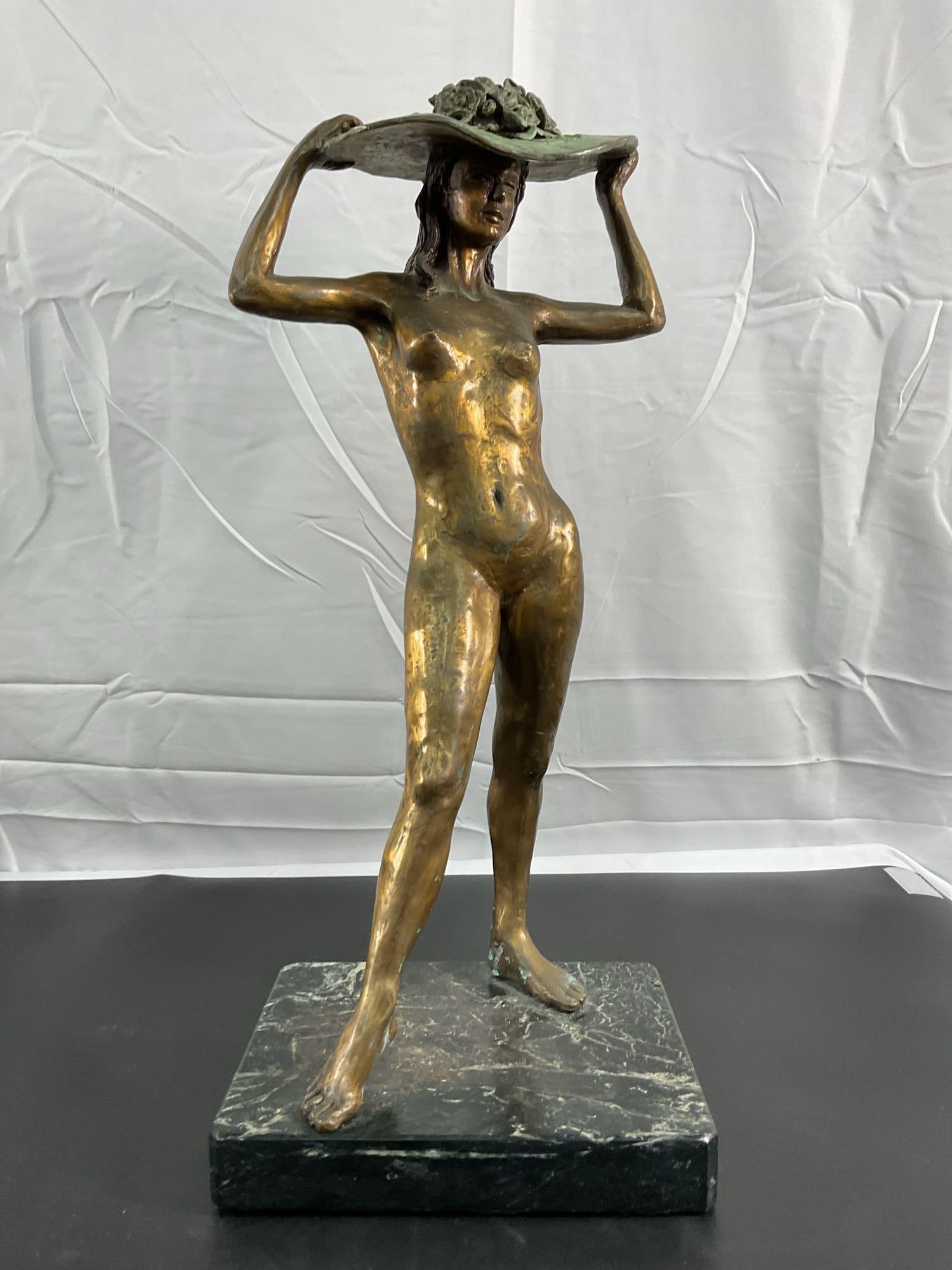 Bronze Sculpture of a Woman with a Floral Hat: This elegant bronze sculpture features a nude woman holding a wide-brimmed hat adorned with detailed flowers. The figure's posture is natural and relaxed, with a sense of movement conveyed through her